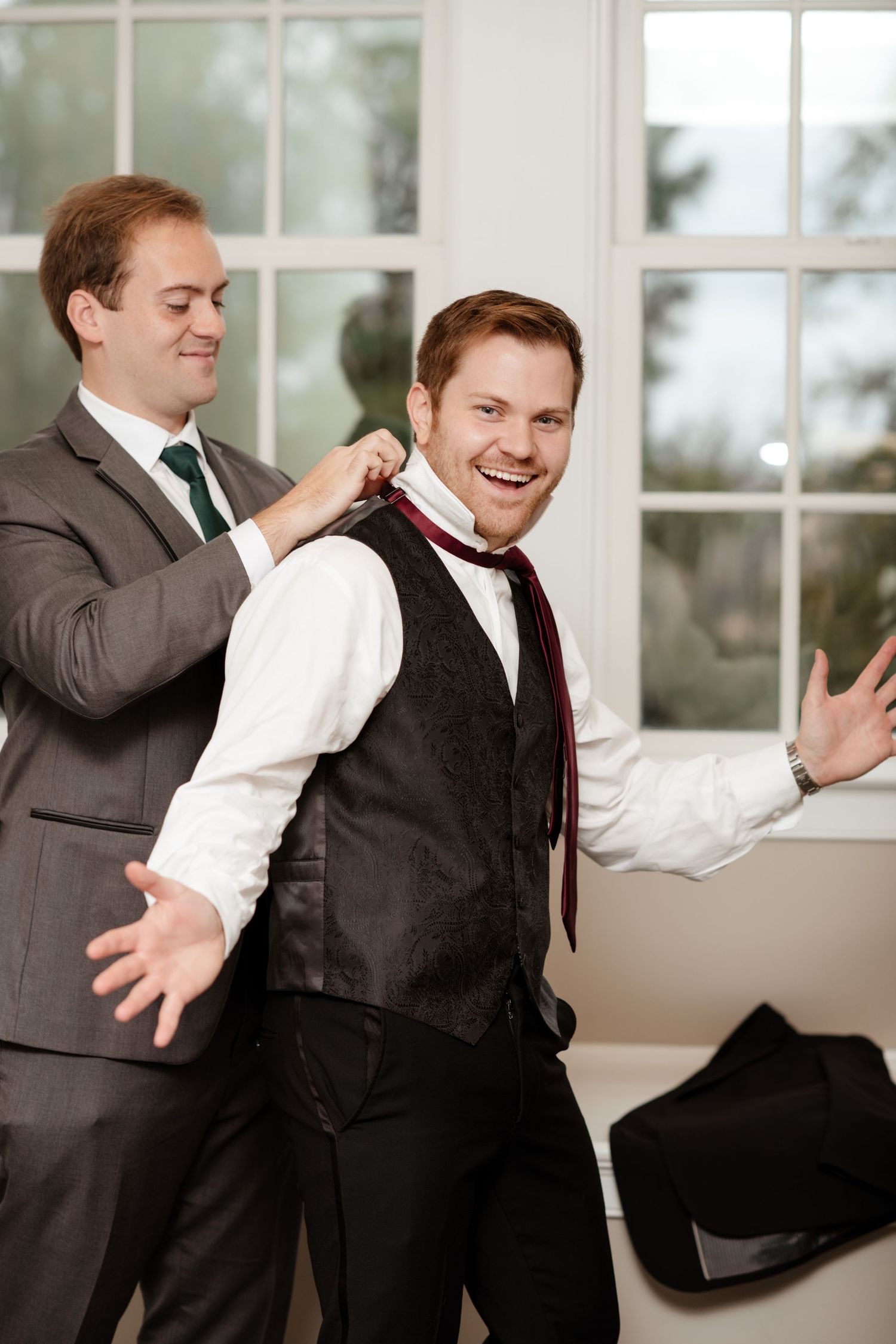 Wedding preparation scene showing formal attire adjustments in bright indoor setting.