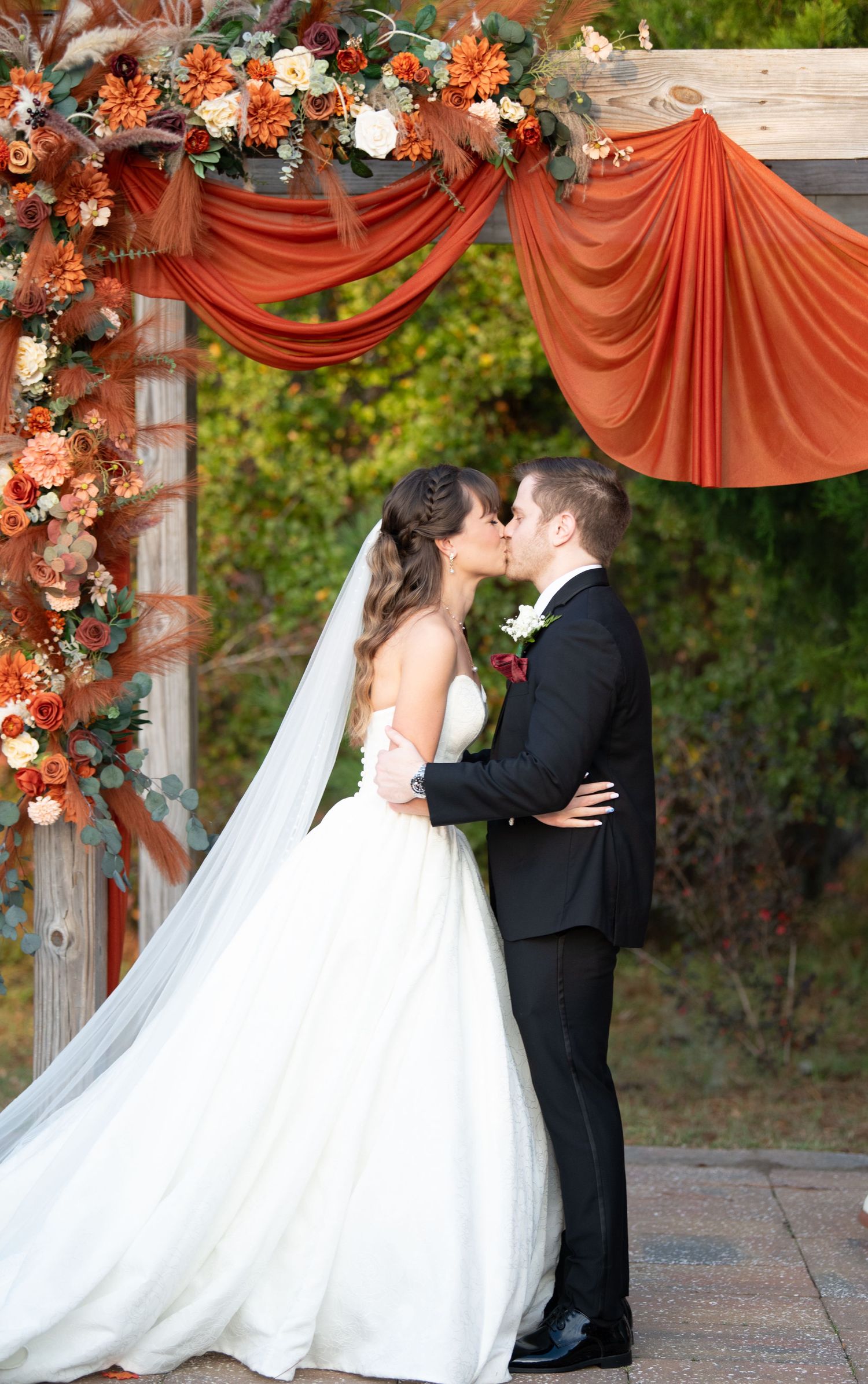 Newlyweds share their first kiss under an elegant coral-draped wedding arch with floral decorations.