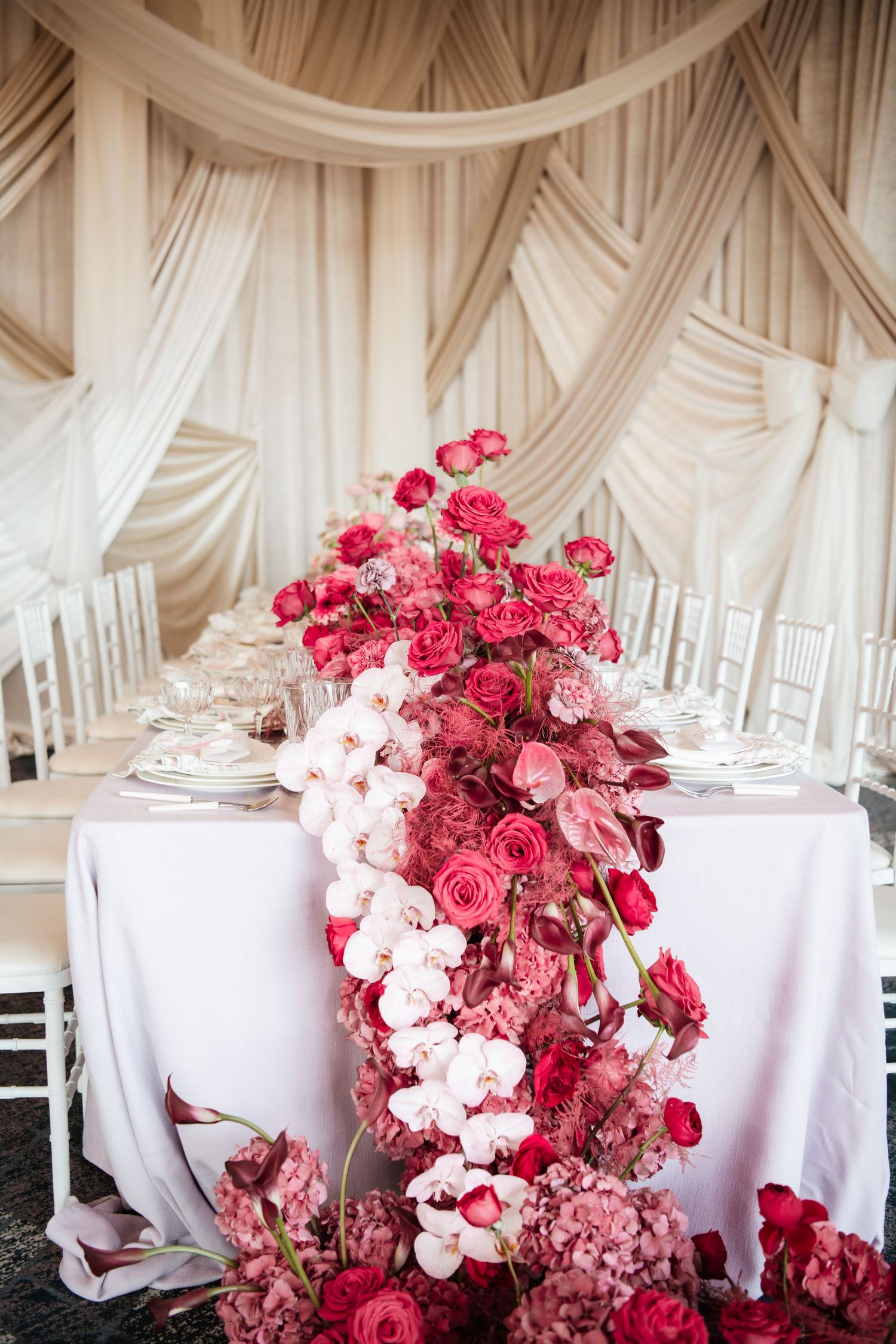 Dramatic floral arrangement with pink roses and white orchids cascading down wedding table.