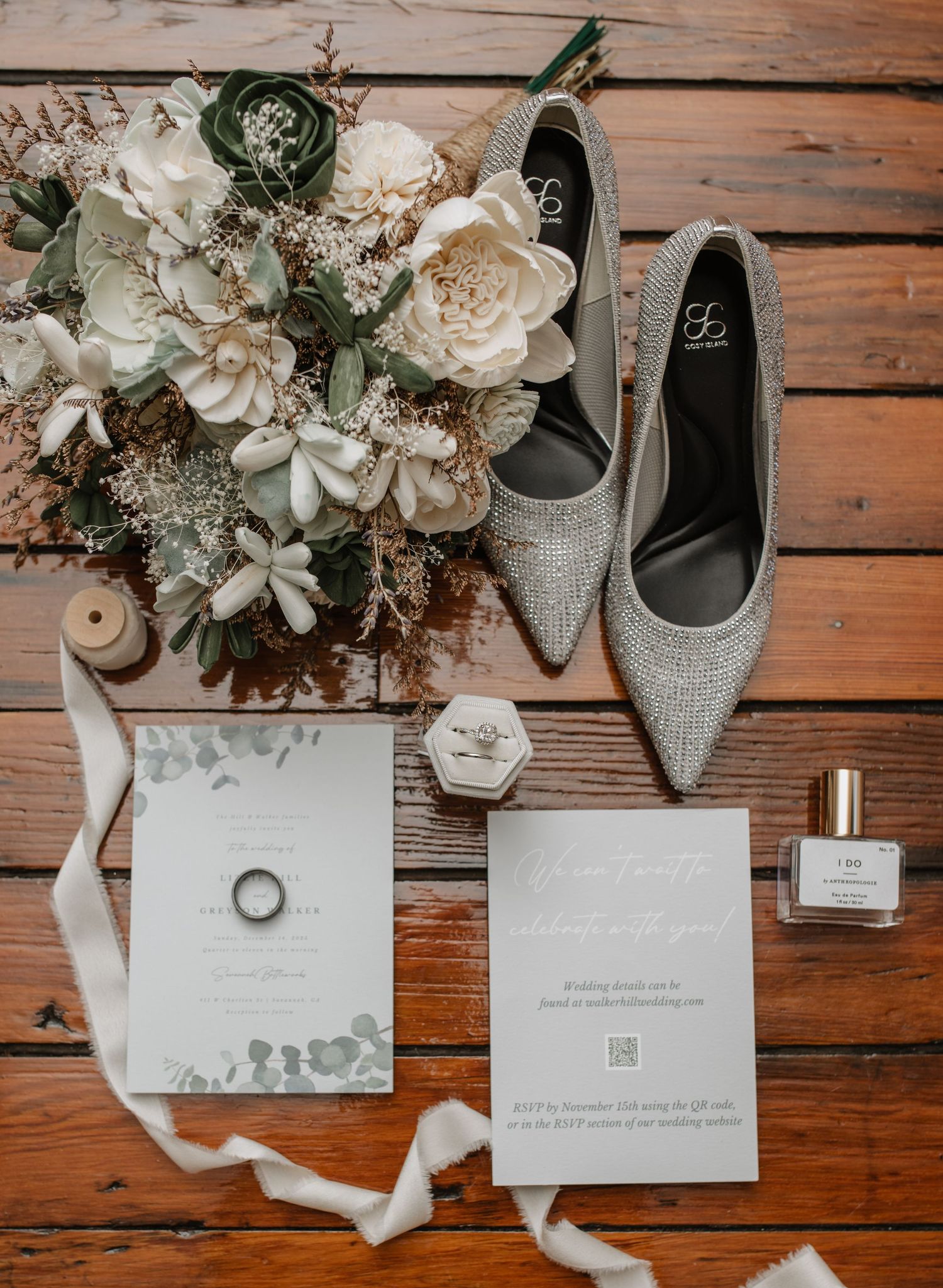 Wedding flat lay with sparkly heels, white flowers, invitation and ring on wooden background.