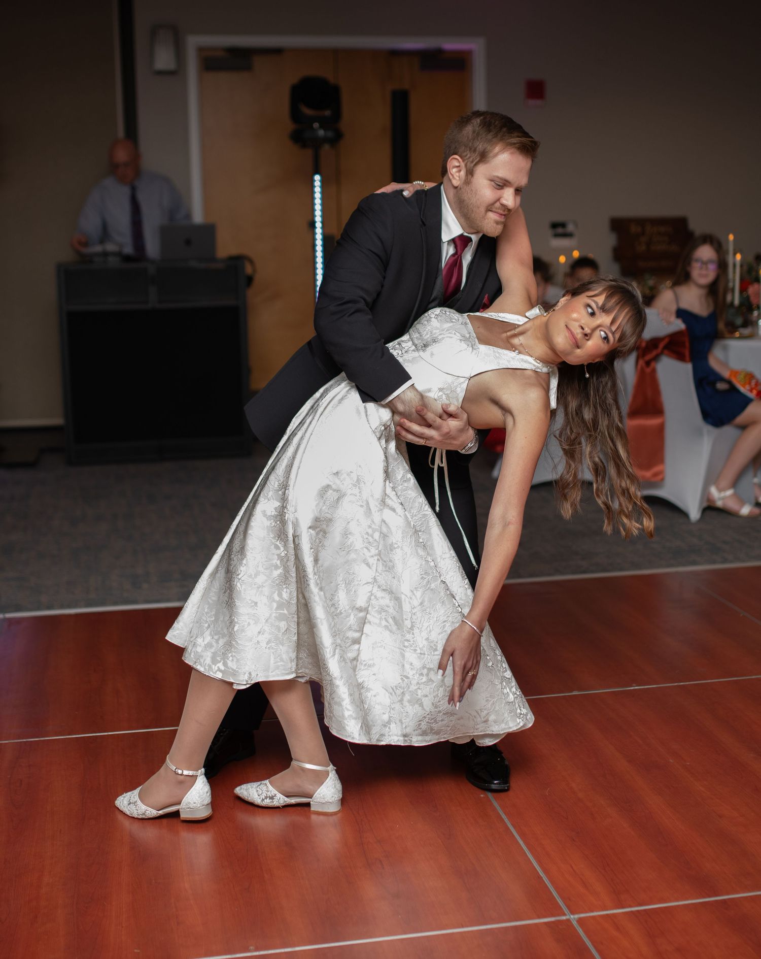 Couple performing a romantic dance dip move on a wooden dance floor at their wedding reception.