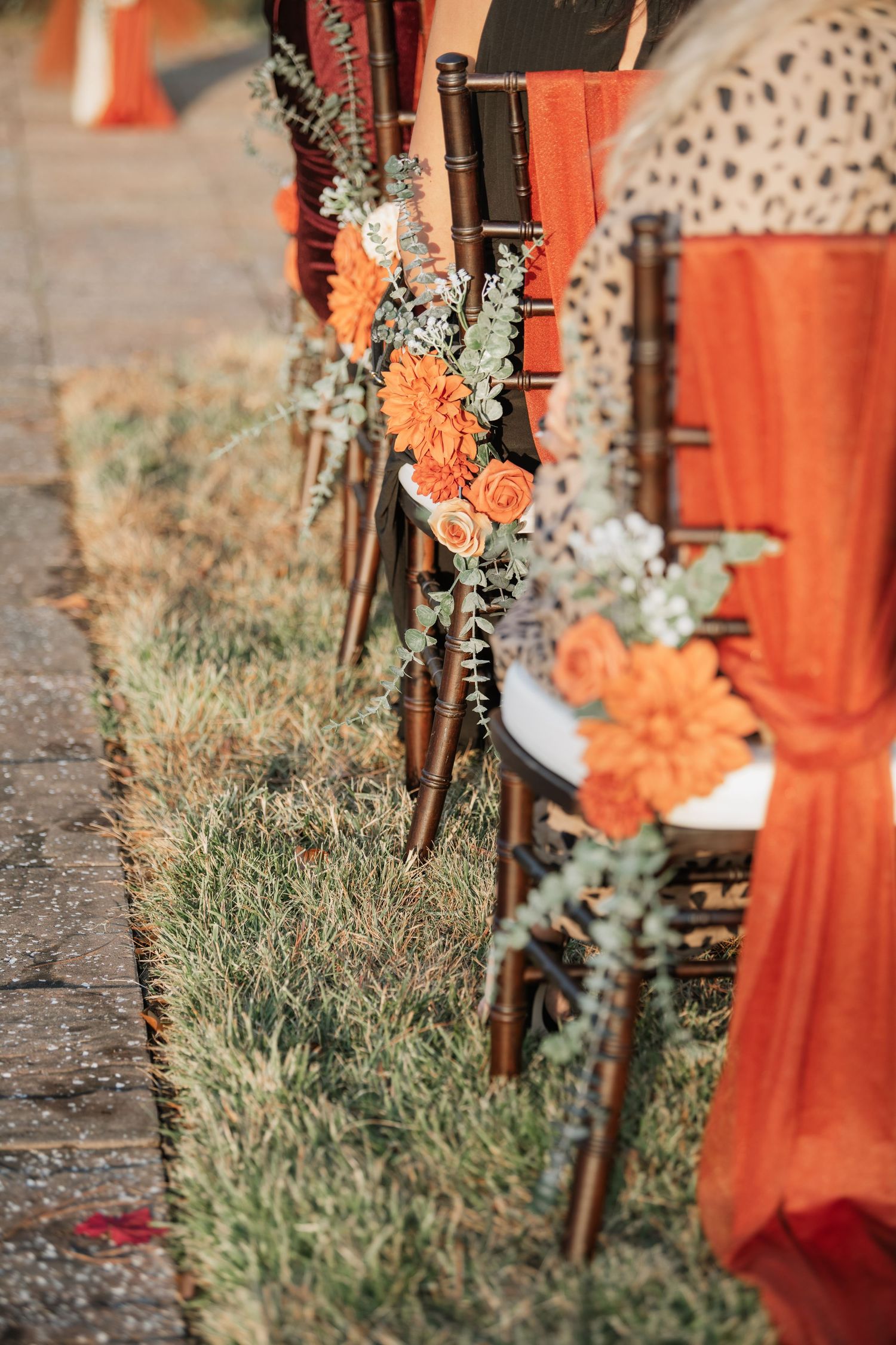 Decorative wedding aisle markers with coral fabric and floral arrangements against natural grass.
