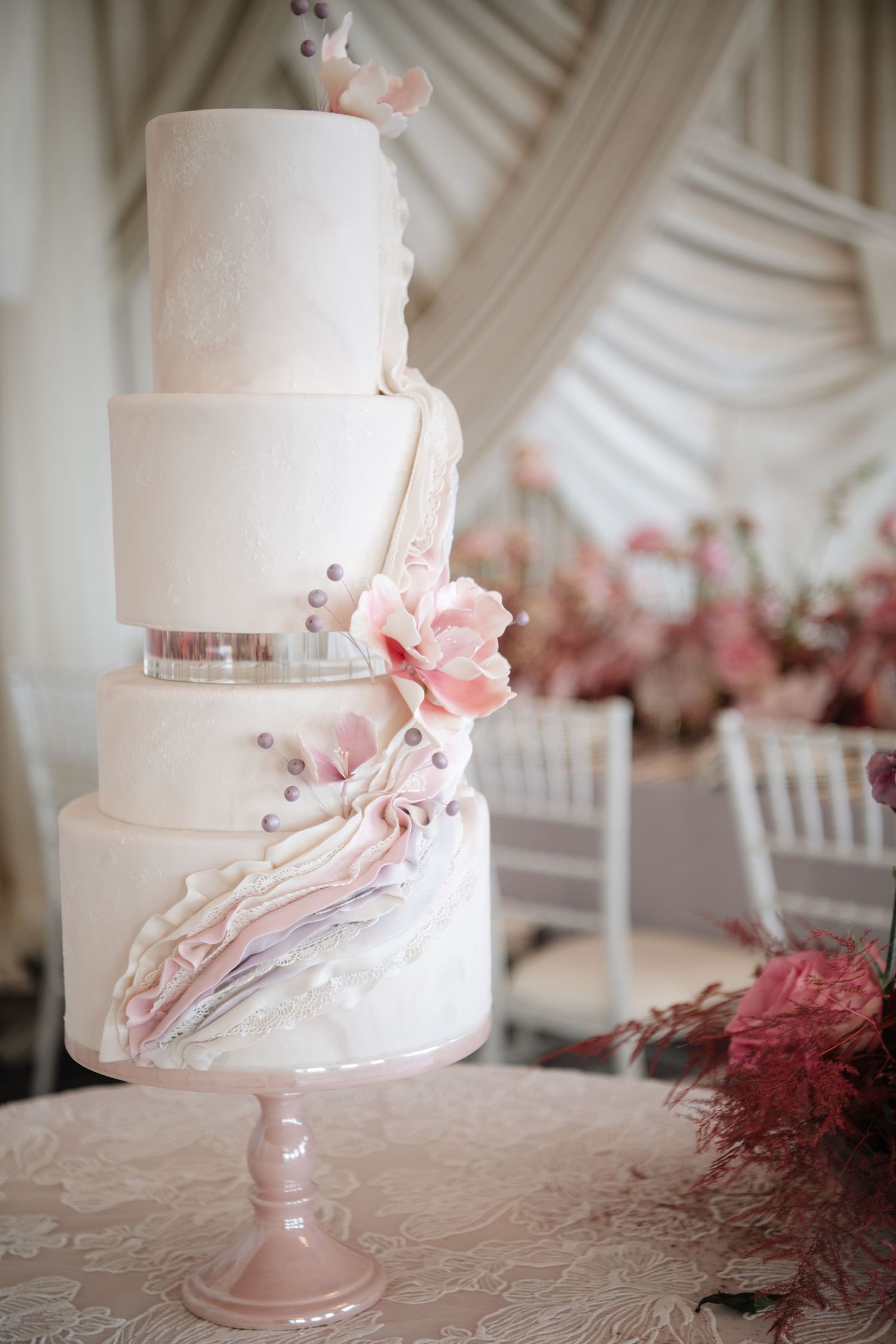 White tiered wedding cake with delicate pink marble design and floral accents on a pink stand.