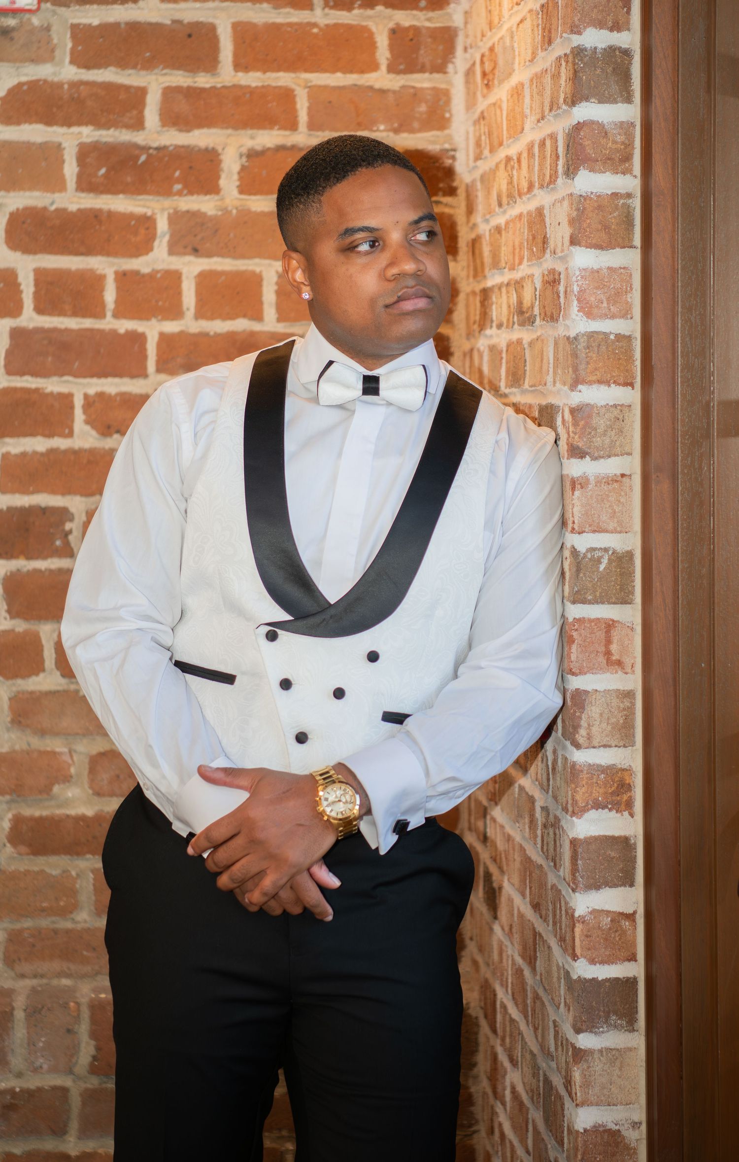 Groomsmen in white tuxedo jackets with black lapels and bow ties pose against brick wall.