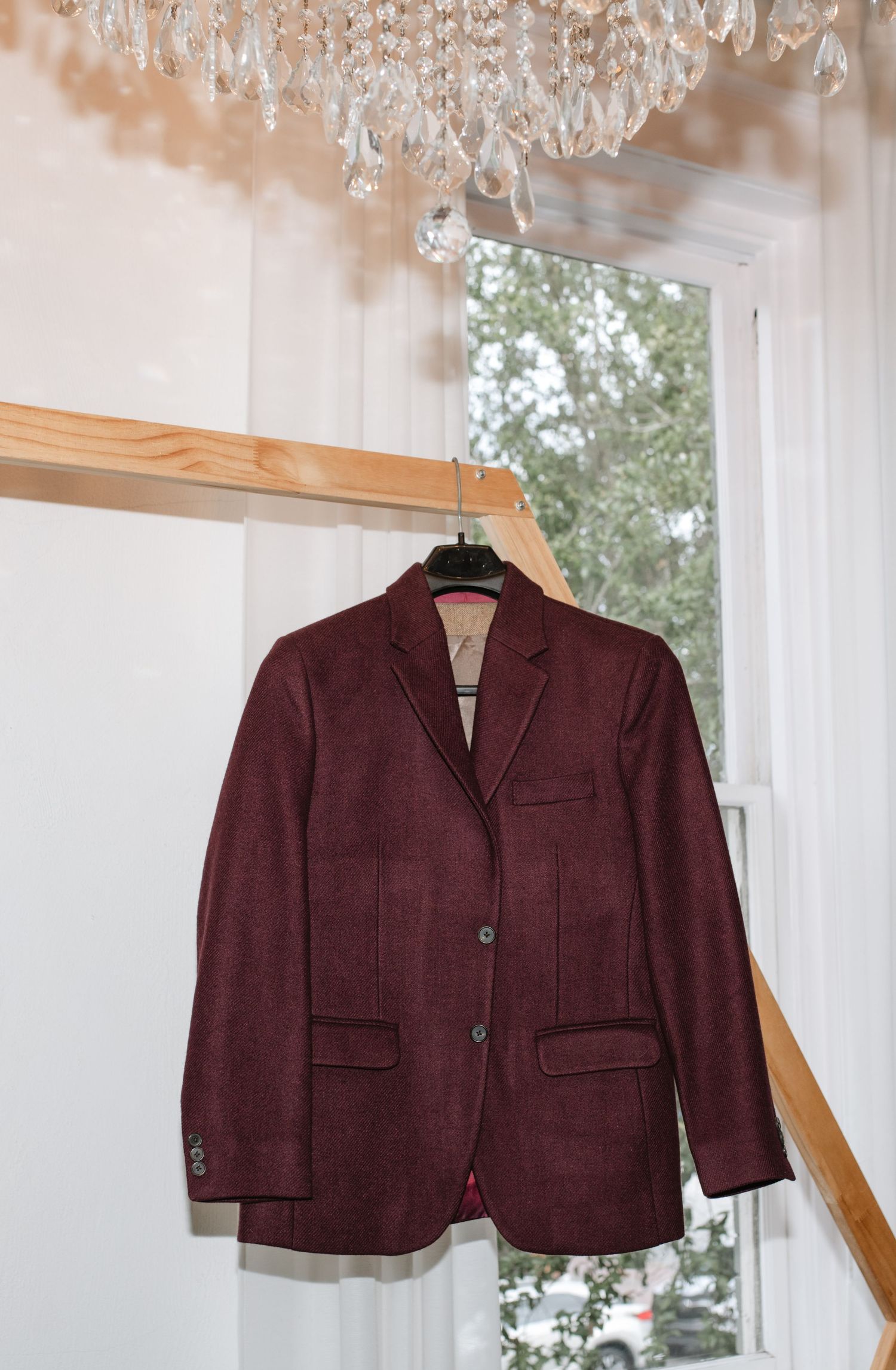 Burgundy suit jacket hanging under crystal chandelier in bright white room.