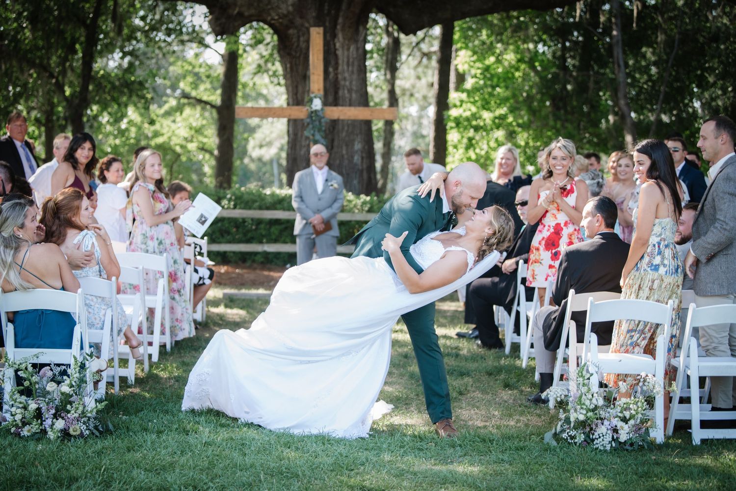 Wedding guests seated outdoors on white chairs during an outdoor ceremony.