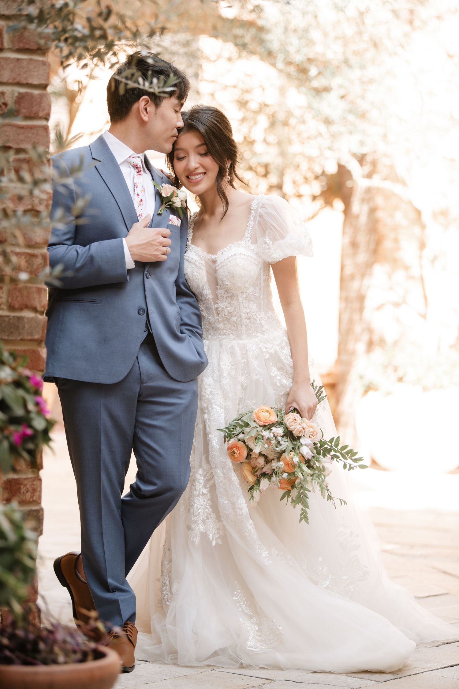 Wedding couple sharing sweet moments in a garden setting with brick architecture.