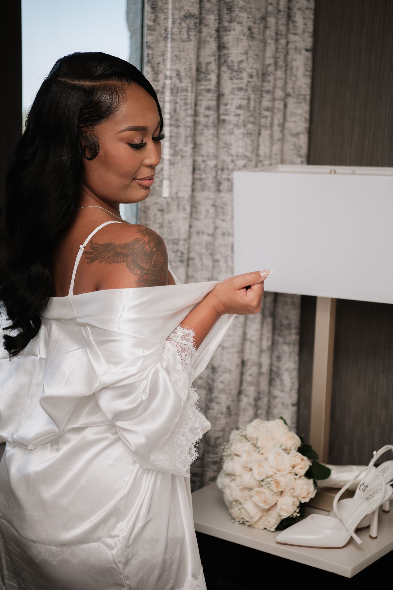 Artistic bridal preparation photo with white heels and roses against textured wall.