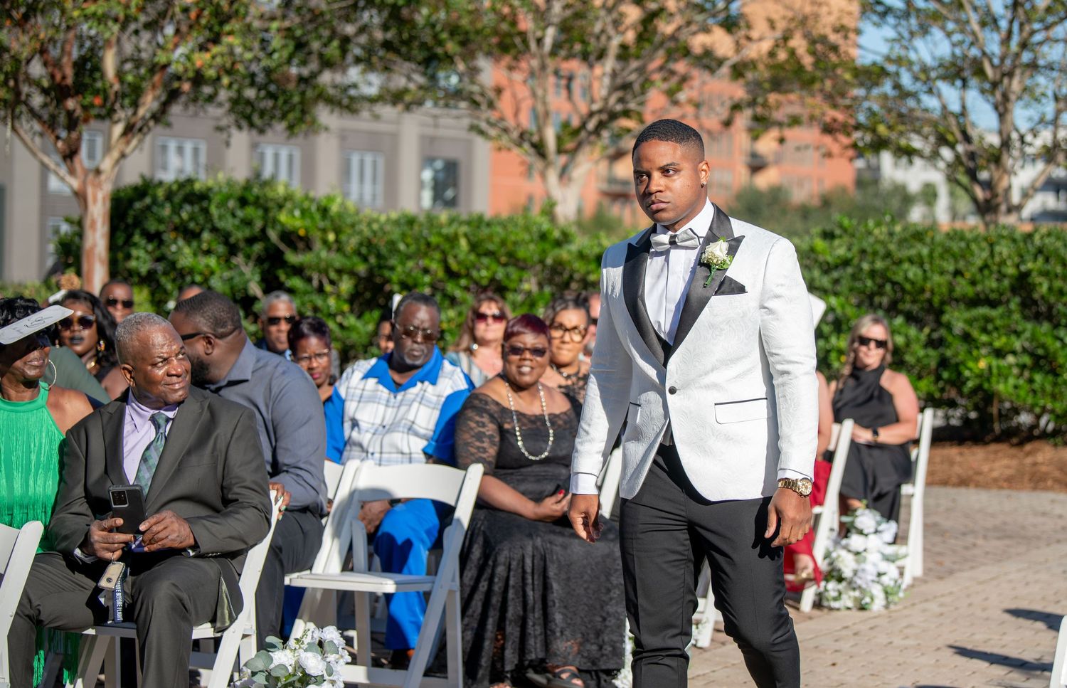 Wedding ceremony setup with white chairs and floral arrangements against brick building.