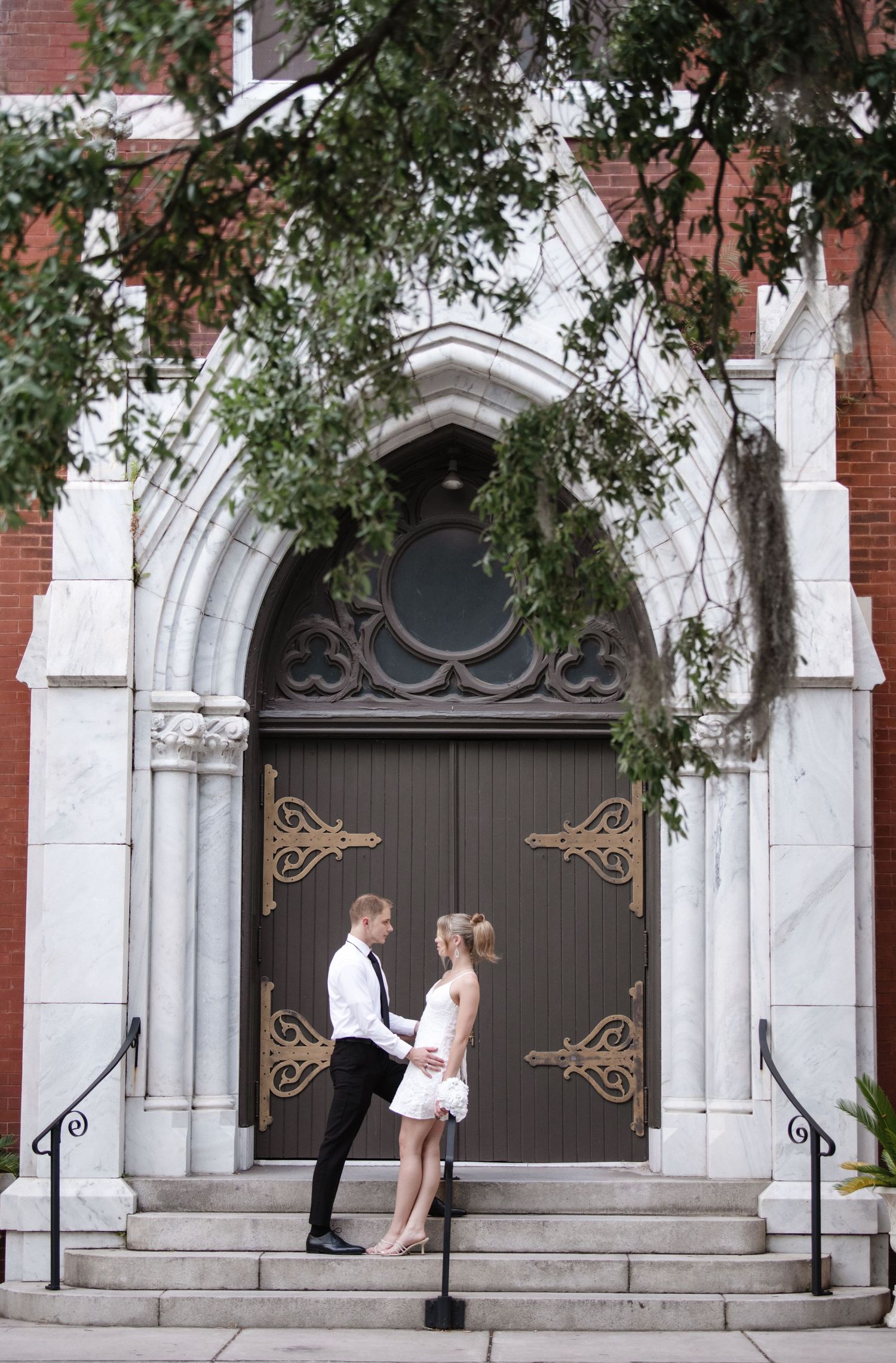 A couple poses romantically in front of an ornate church door with gothic architecture.