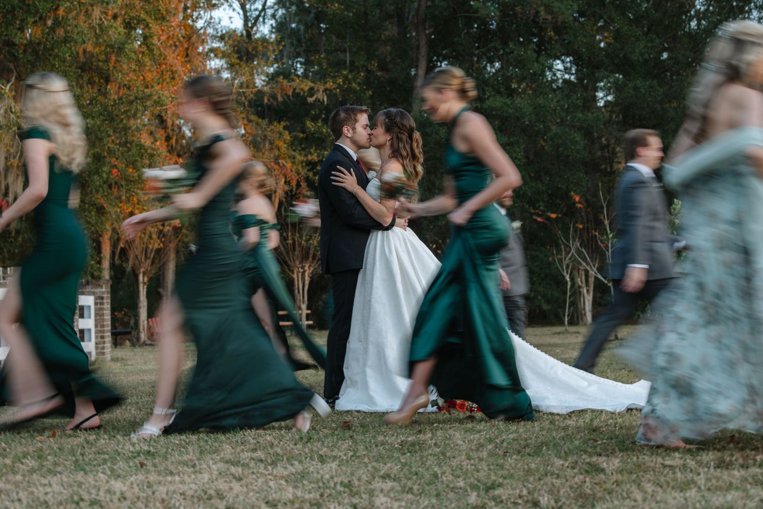 Wedding party running and laughing together in an outdoor setting with green dresses and gray suits.