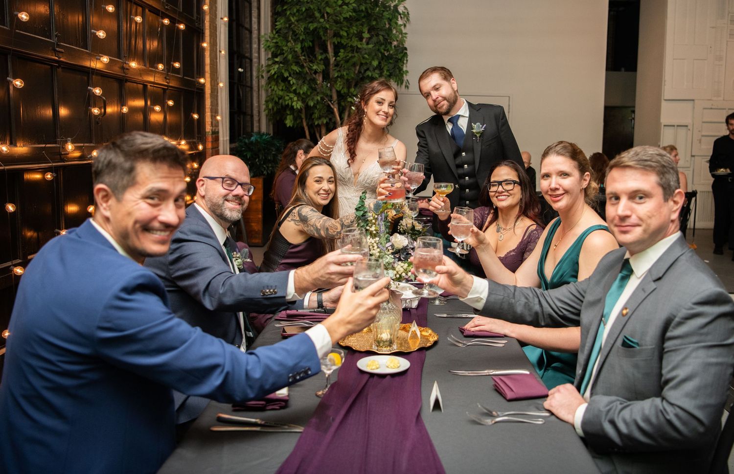 Wedding reception guests celebrating and toasting at decorated dining tables.