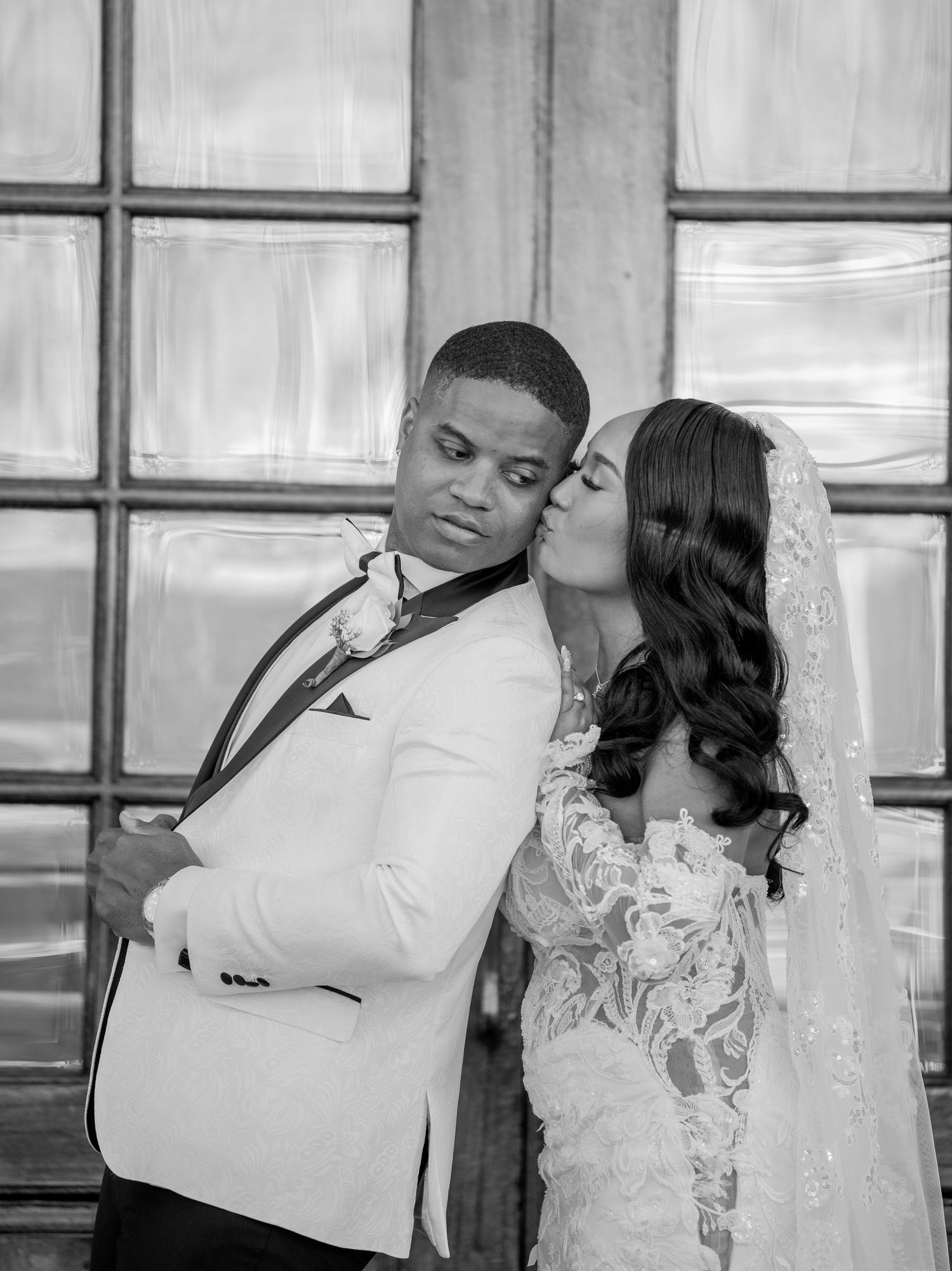 Romantic black and white wedding portrait series showing intimate moments between newlyweds against a window backdrop.