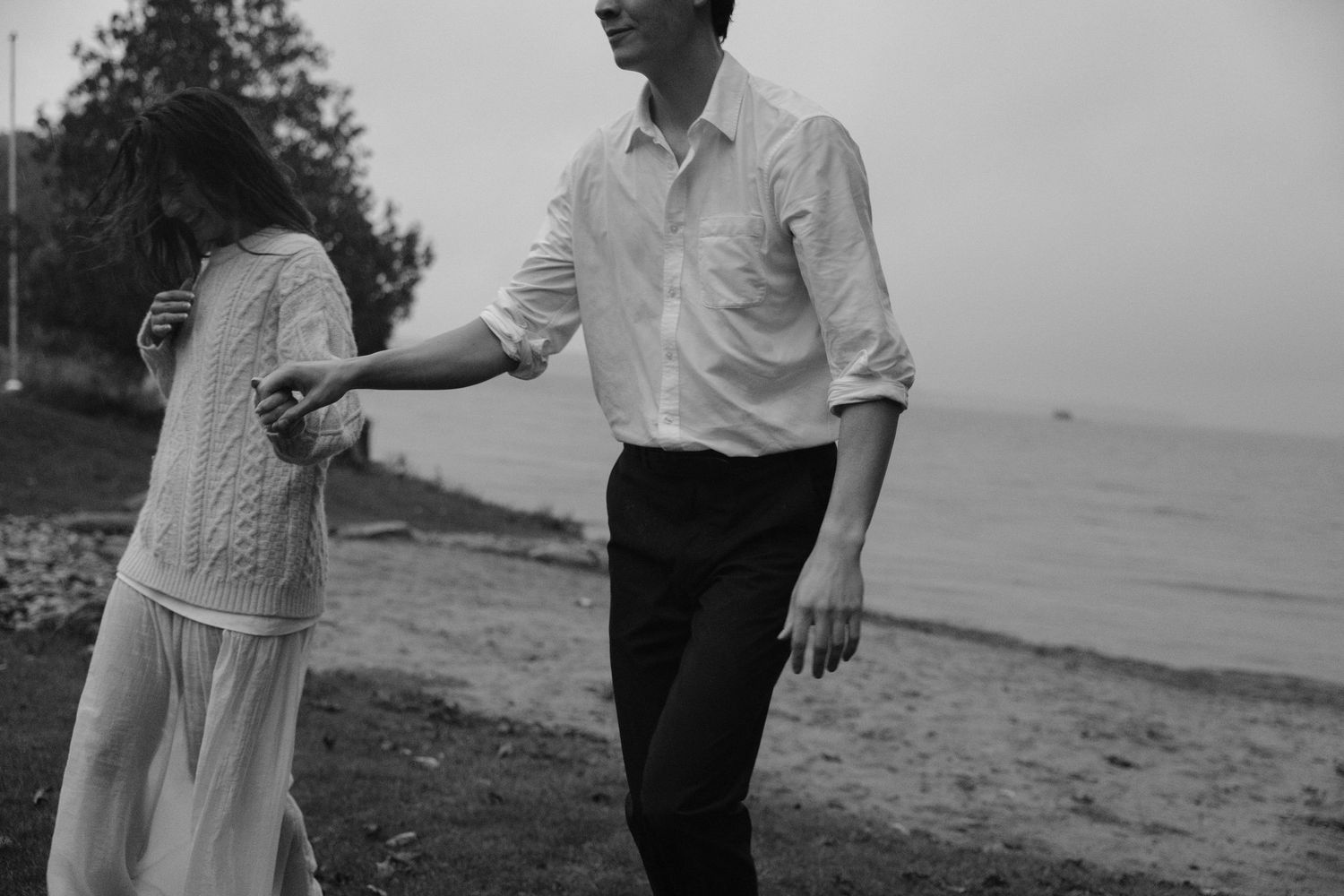 Black and white couple holding hands walking along misty beach shoreline.