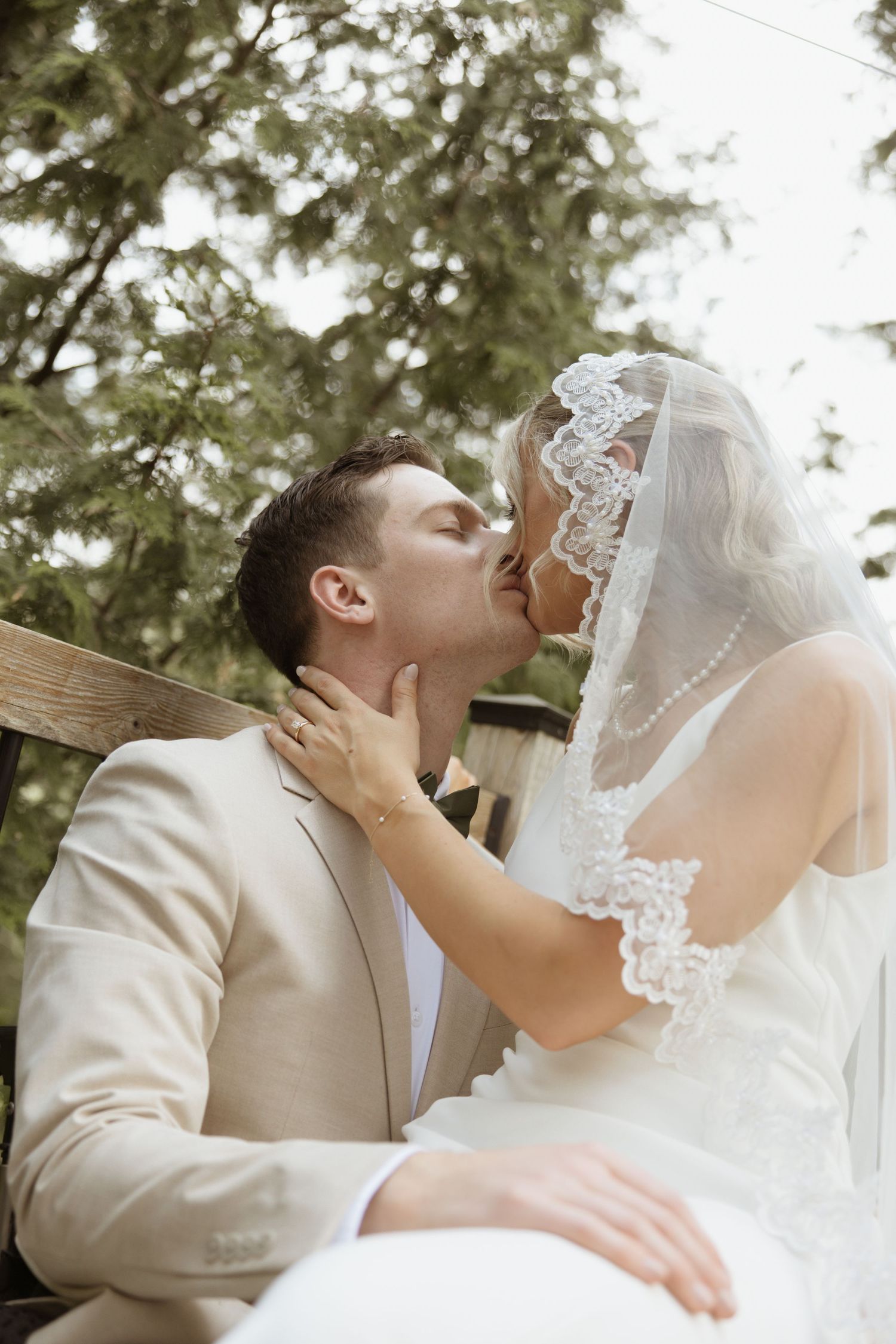 Bride and groom sharing a kiss outdoors with evergreen trees in background.