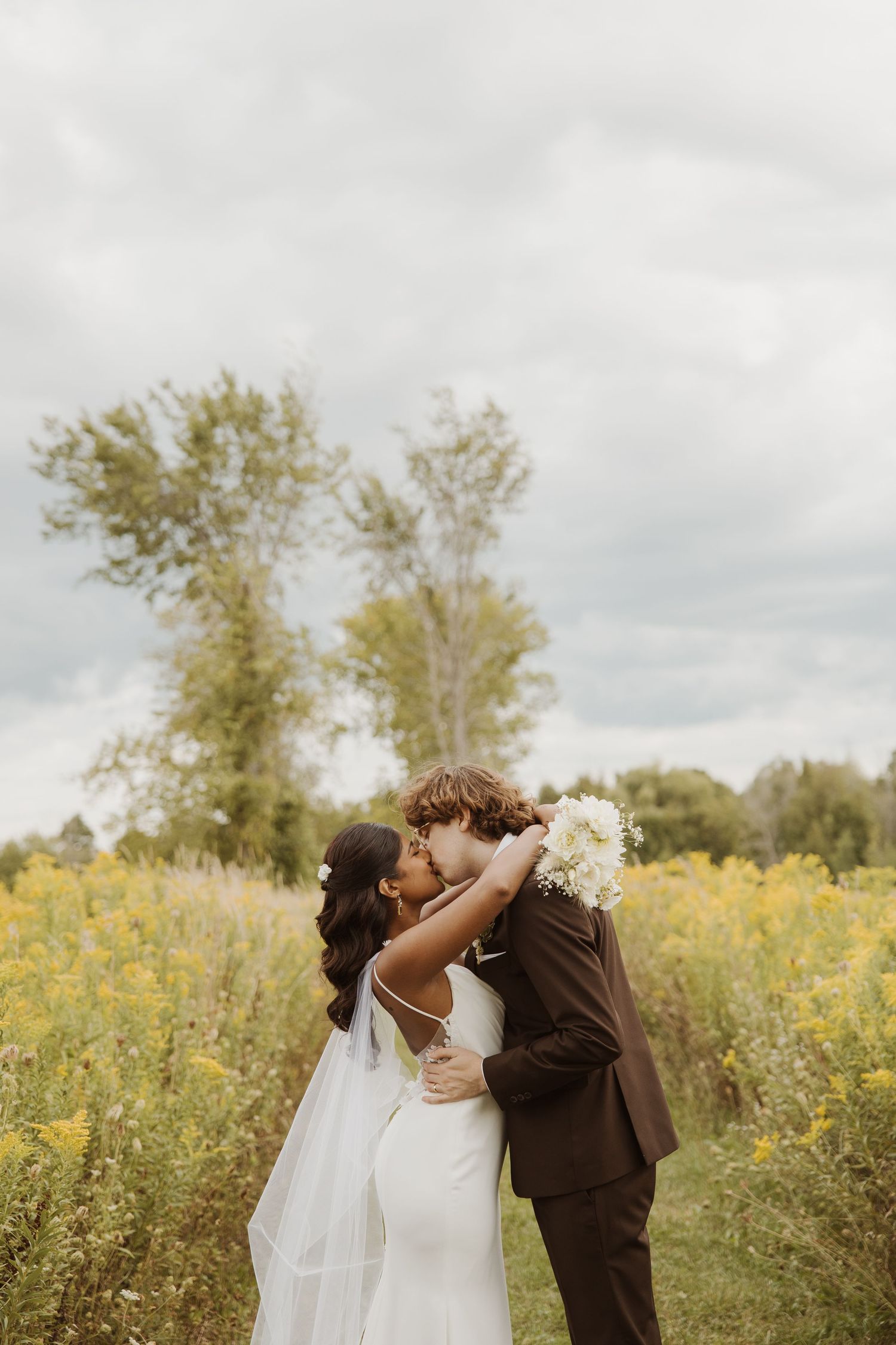 Bride and groom sharing a romantic kiss in a golden wildflower field on their wedding day.