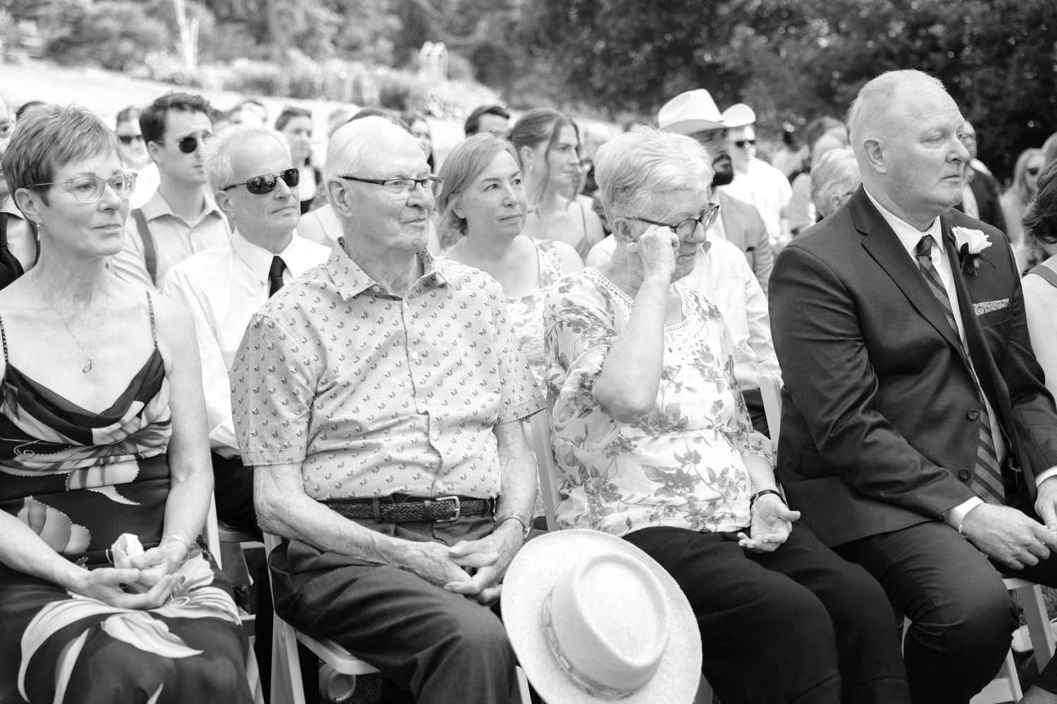 Black and white photo of emotional wedding guests seated during an outdoor ceremony.