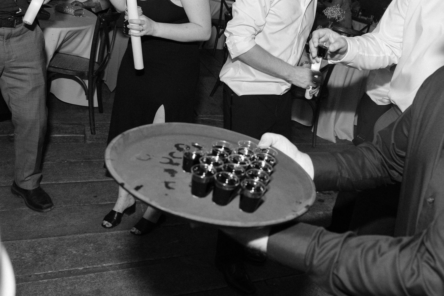 Wedding guests taking shots from a round tray during black and white reception party celebration.