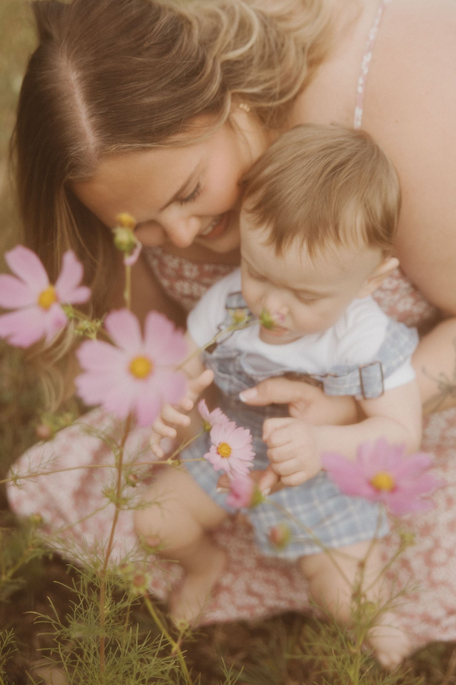 Mother and baby boy exploring pink cosmos flowers together in a soft, dreamy garden setting.