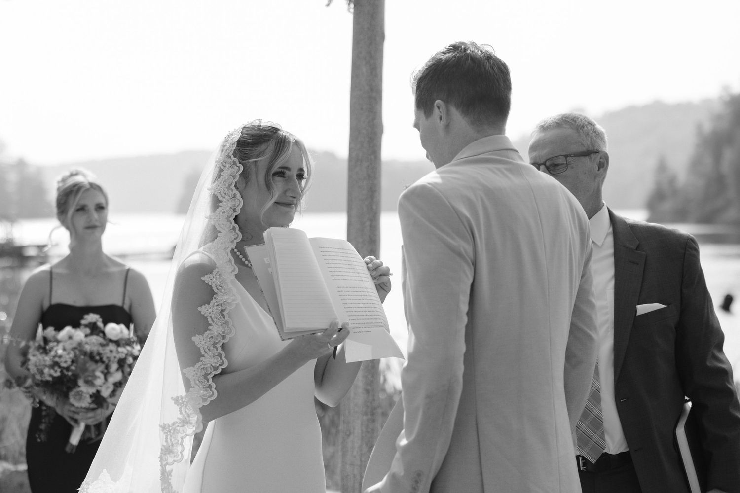 Bride reading vows to groom during outdoor lakeside wedding ceremony.