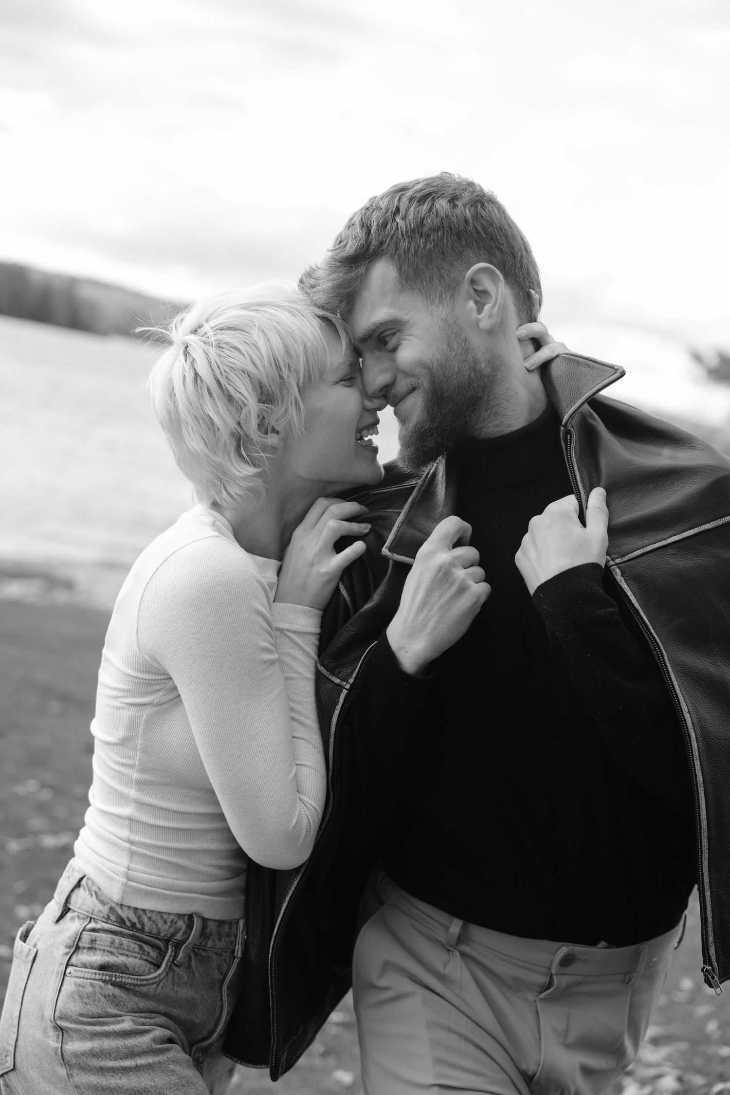 Black and white intimate couple almost kissing outdoors near a lake.