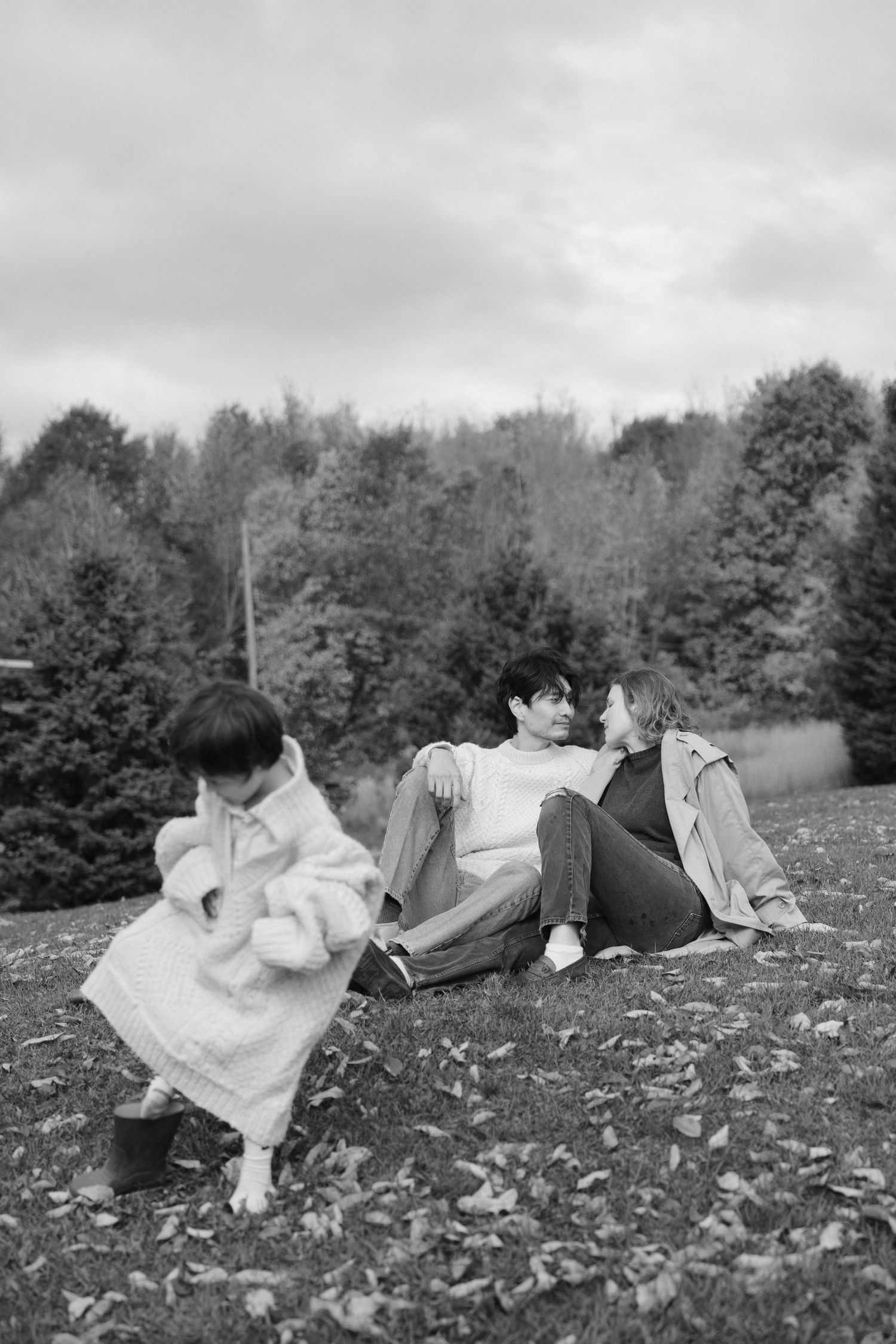 Black and white photo of couple relaxing on grass while child plays nearby.
