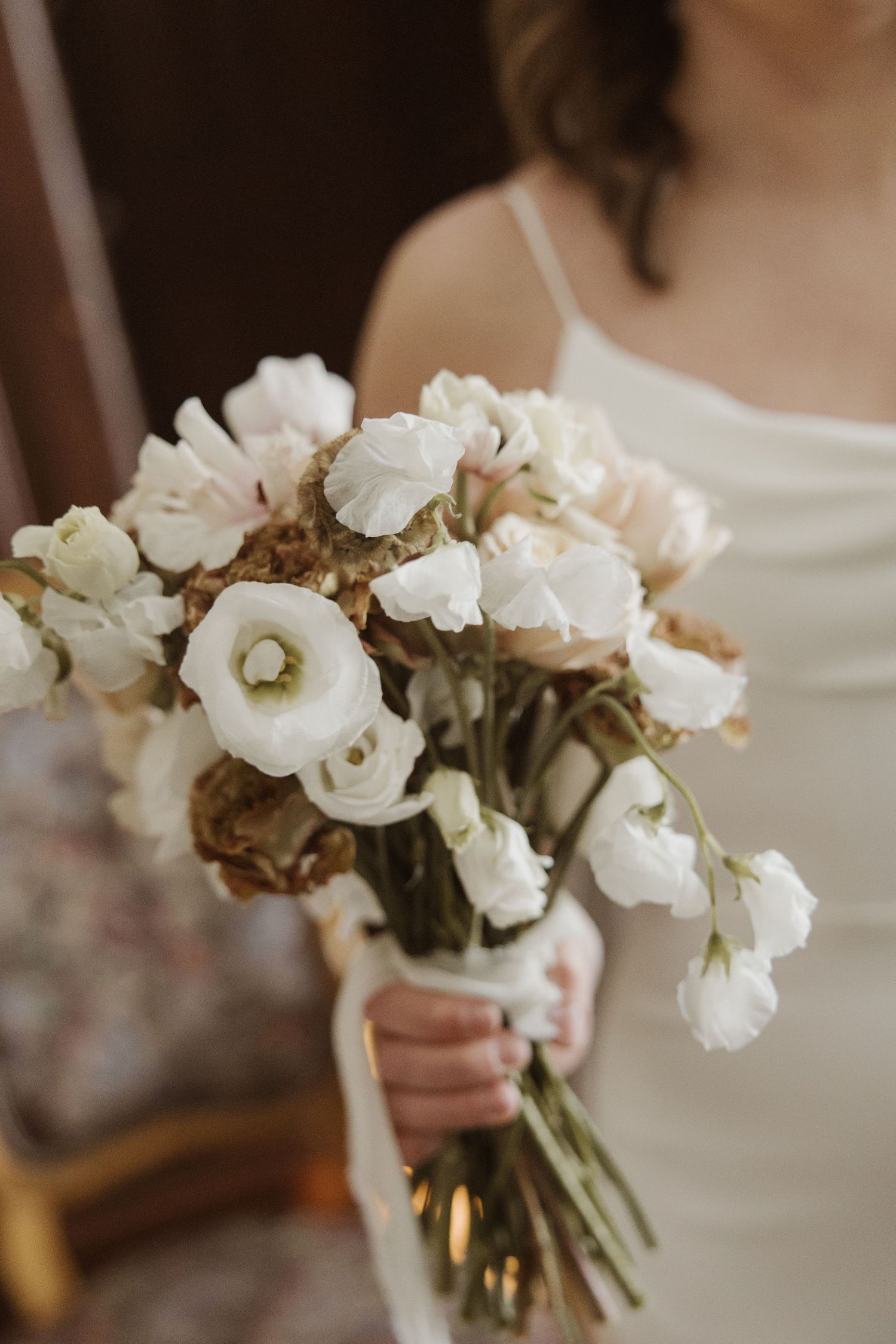 Bride holding bouquet of white lisianthus and blush flowers in white dress.