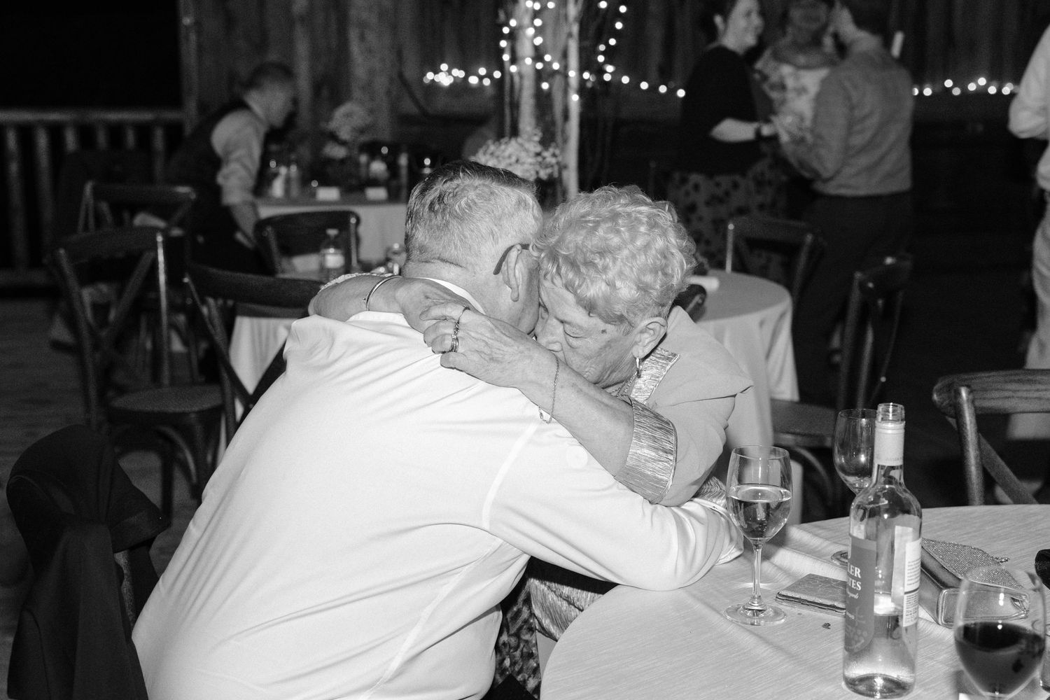 Elderly couple sharing tender intimate moment leaning together at wedding reception dinner table.