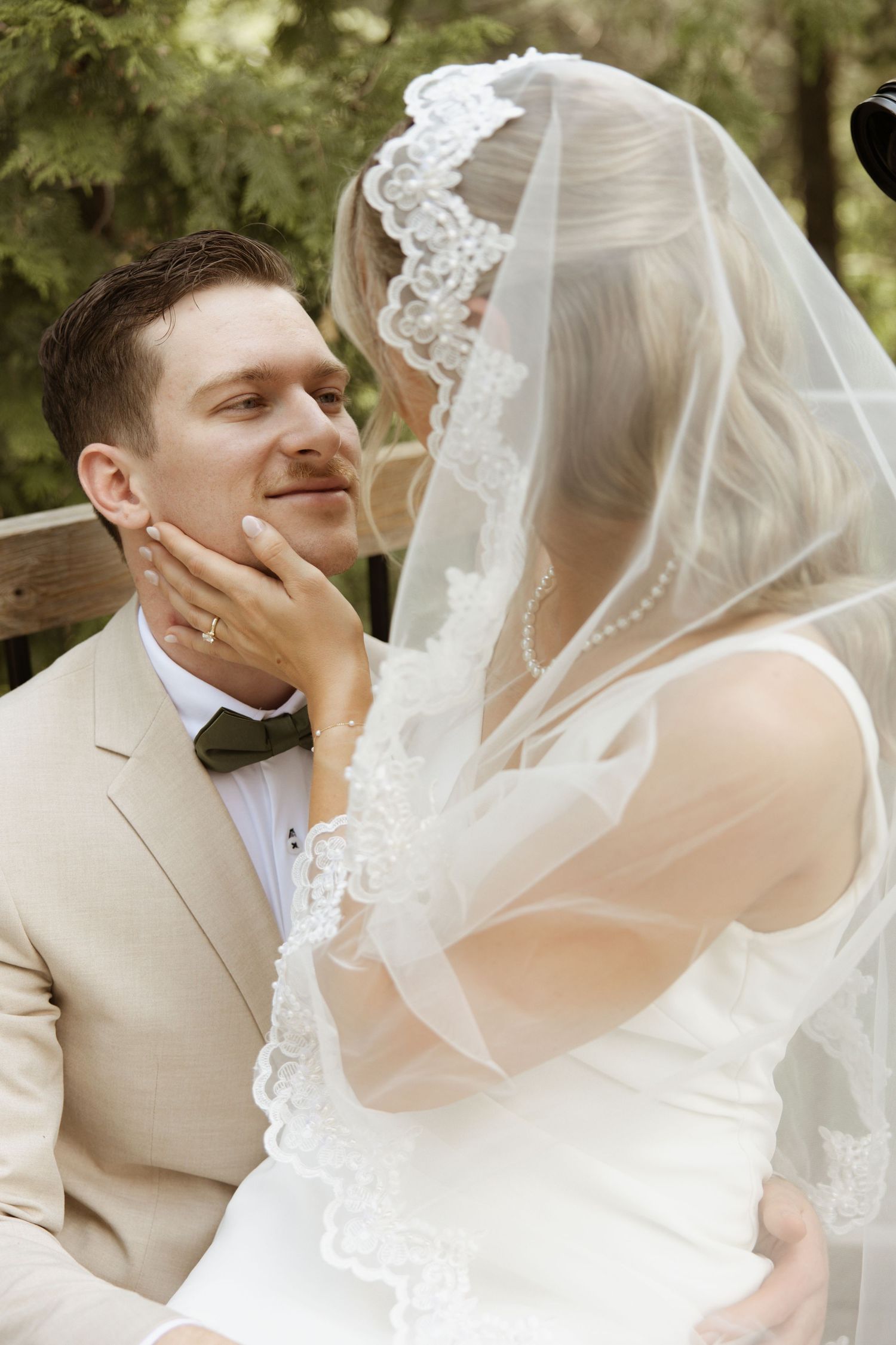 Bride gently cups grooms face as they share an intimate moment, bride wearing ornate lace veil.