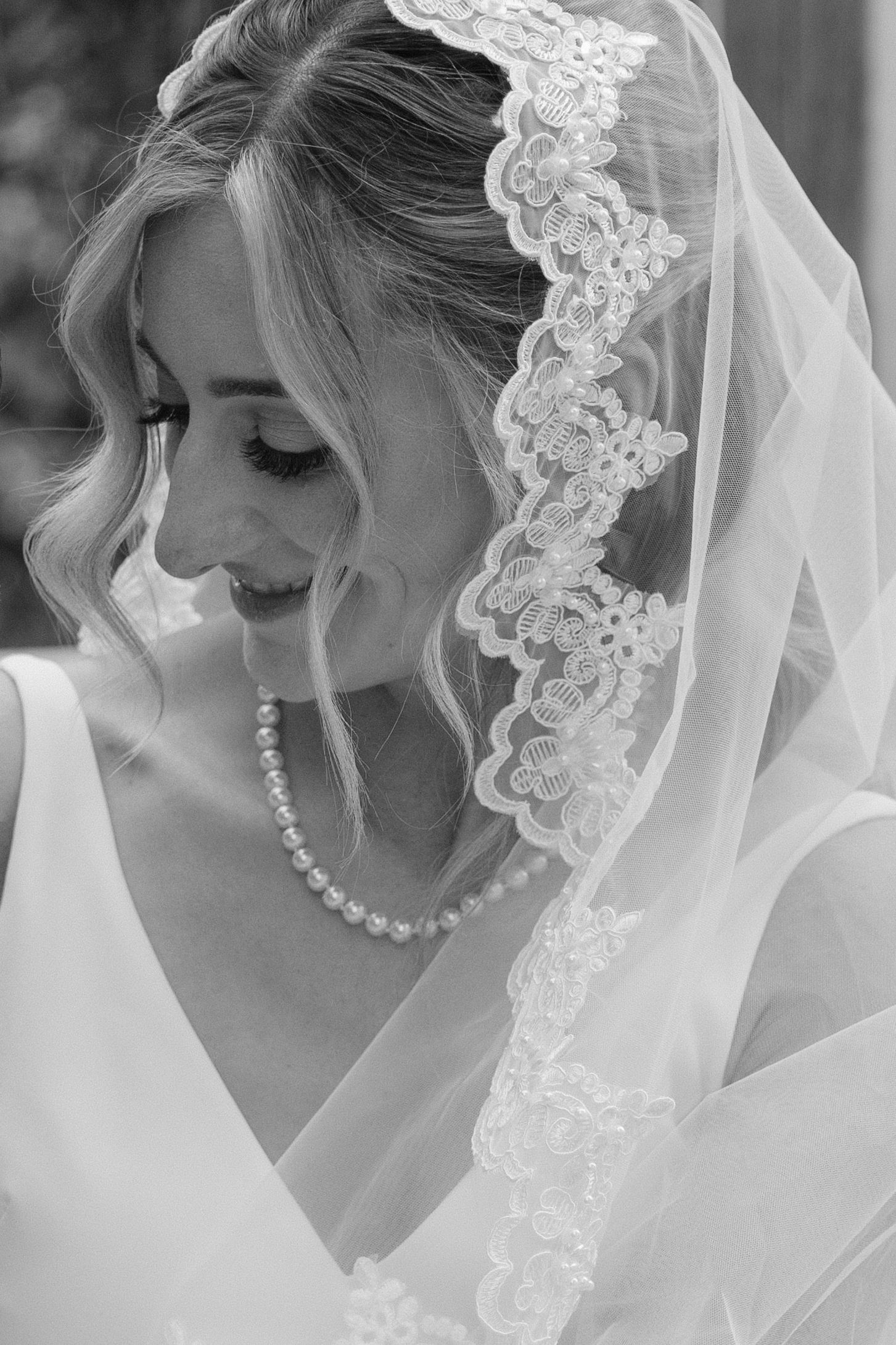 Elegant black and white portrait of bride wearing lace-trimmed veil and pearl necklace.