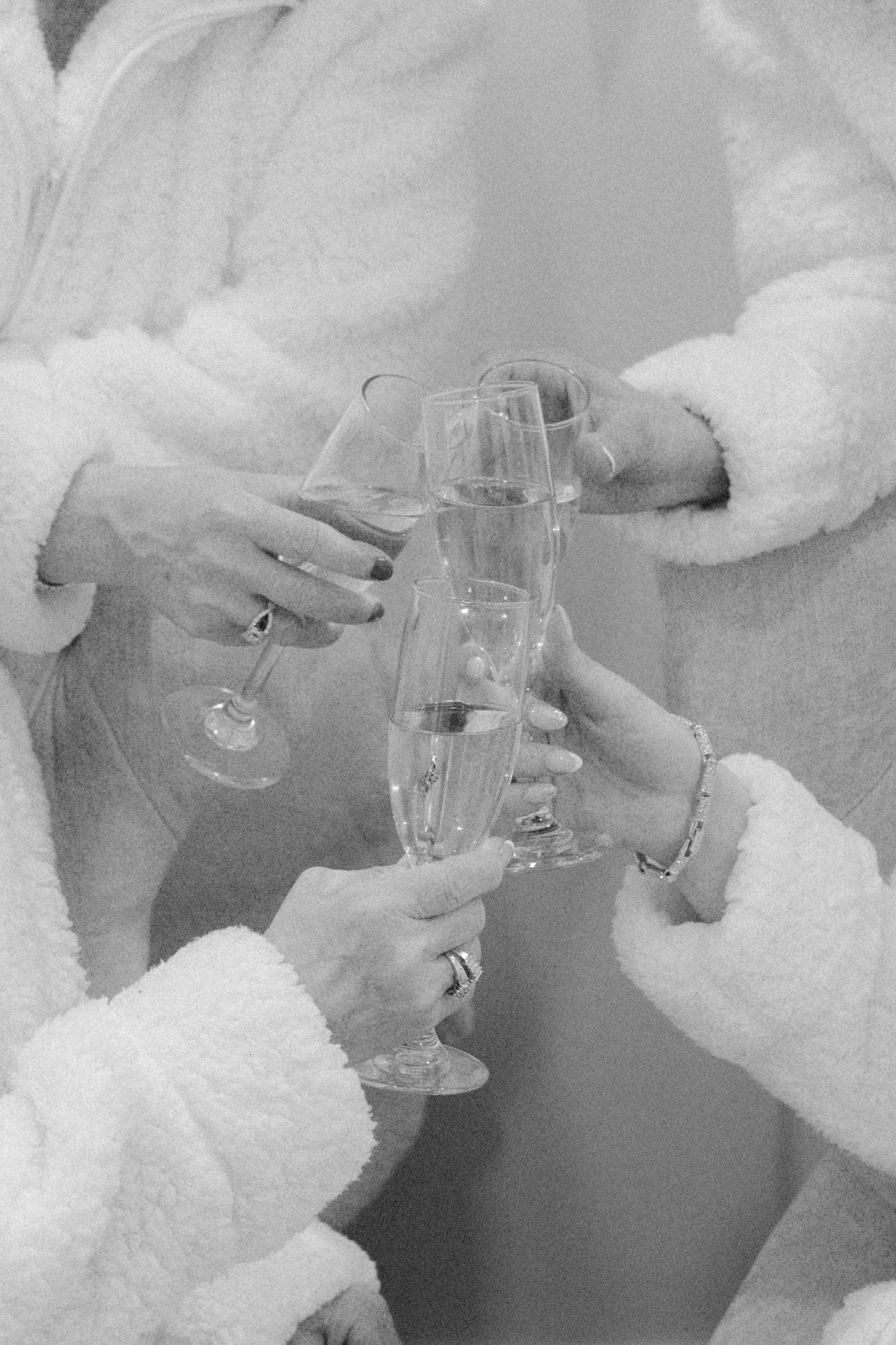 Black and white photo of bridesmaids in white robes toasting with champagne flutes before the wedding.