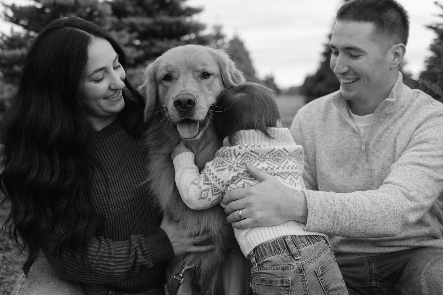Black and white family photo with parents, toddler, and golden retriever dog outdoors.