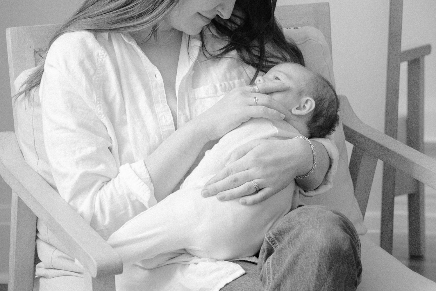 Black and white photo of a mother tenderly cradling her newborn baby while seated in a chair.