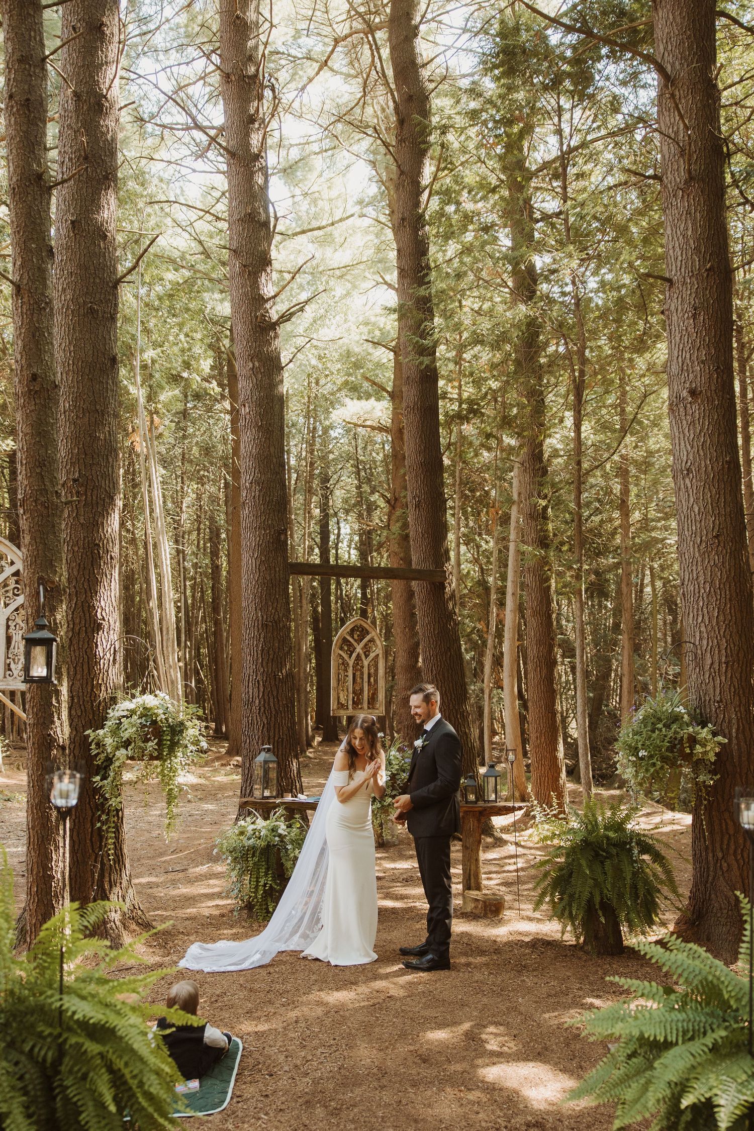 Bride and groom exchanging vows in a stunning outdoor forest ceremony among tall pine trees.