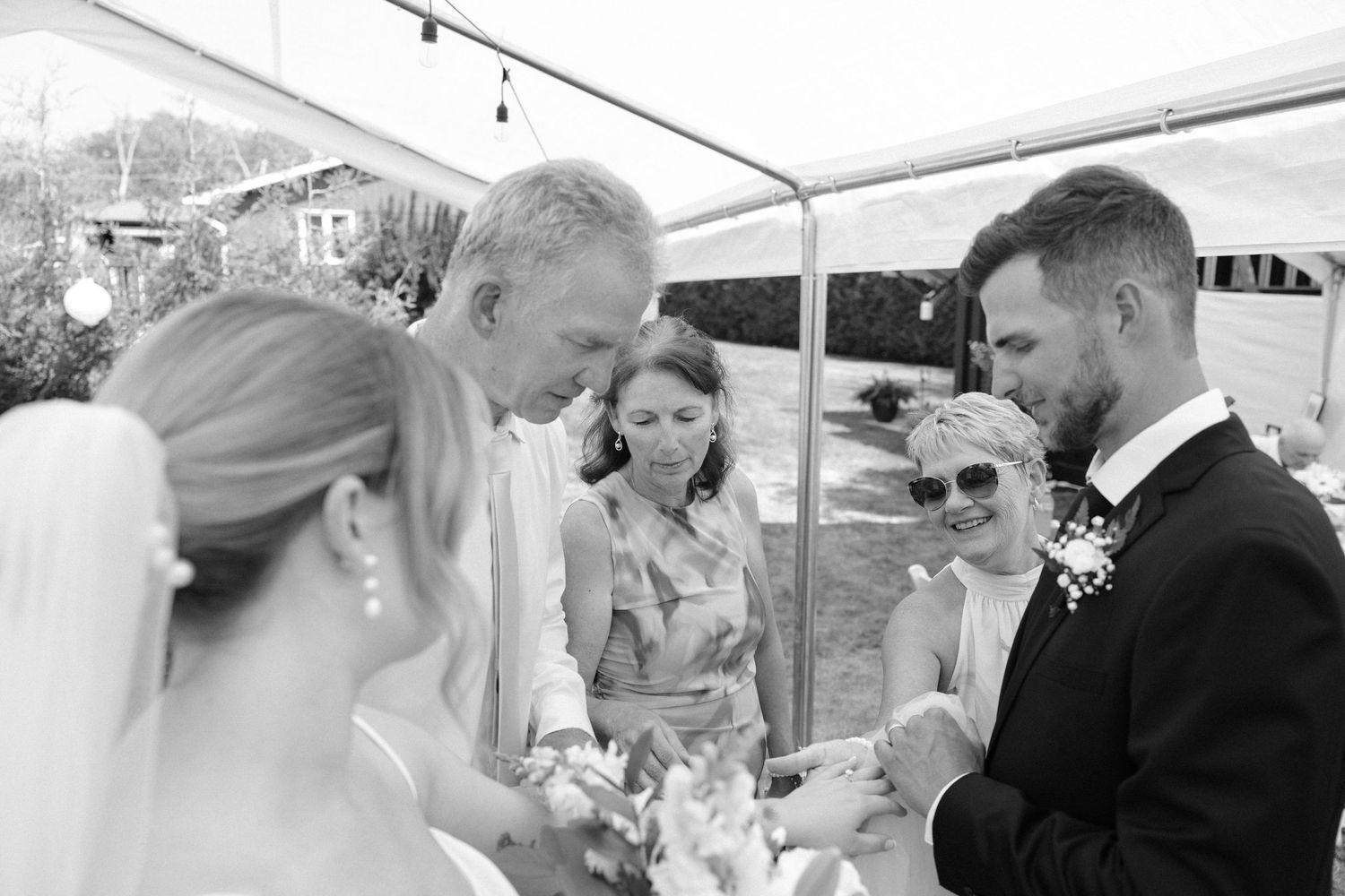 Black and white photo of bride and groom exchanging rings during outdoor wedding ceremony.