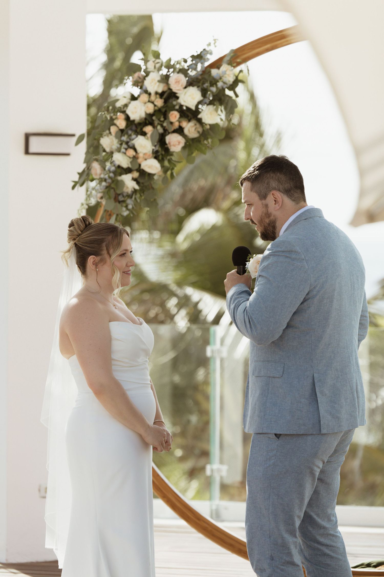 Bride and groom exchanging vows at outdoor wedding ceremony with floral arch backdrop.