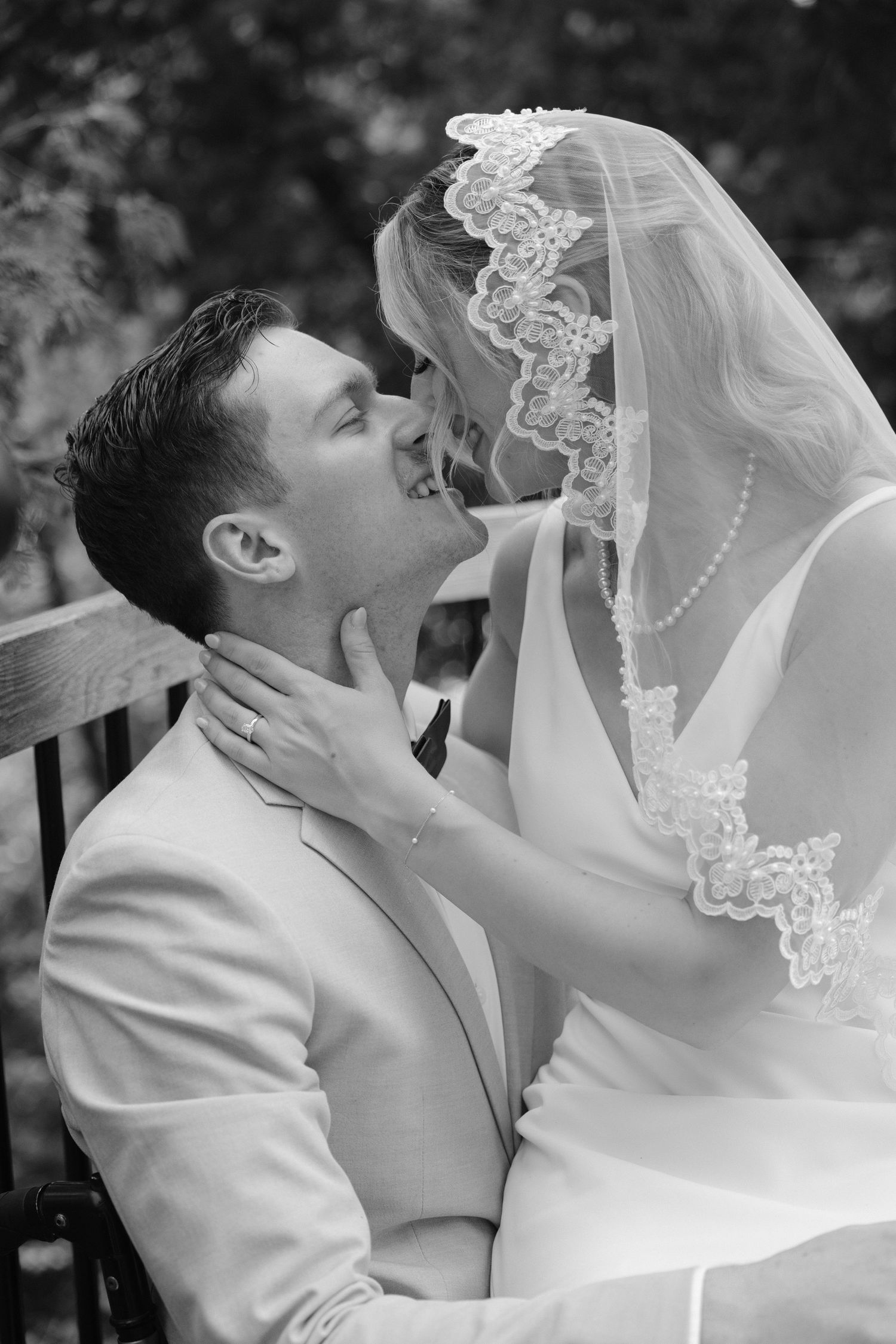 Black and white photo of bride and groom sharing a tender moment, bride in lace veil leaning toward groom.