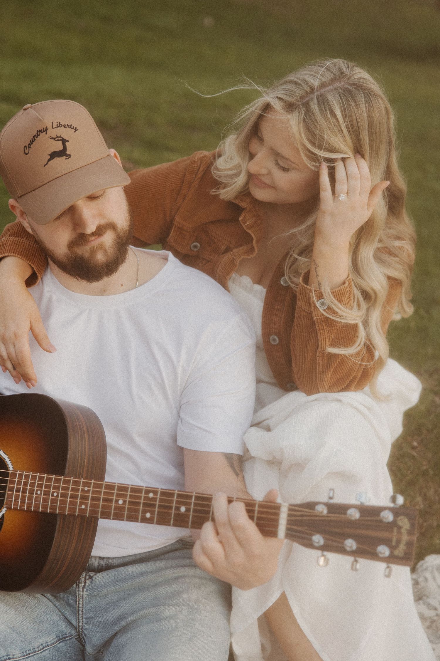Couple sitting closely outdoors as man plays acoustic guitar at golden hour.