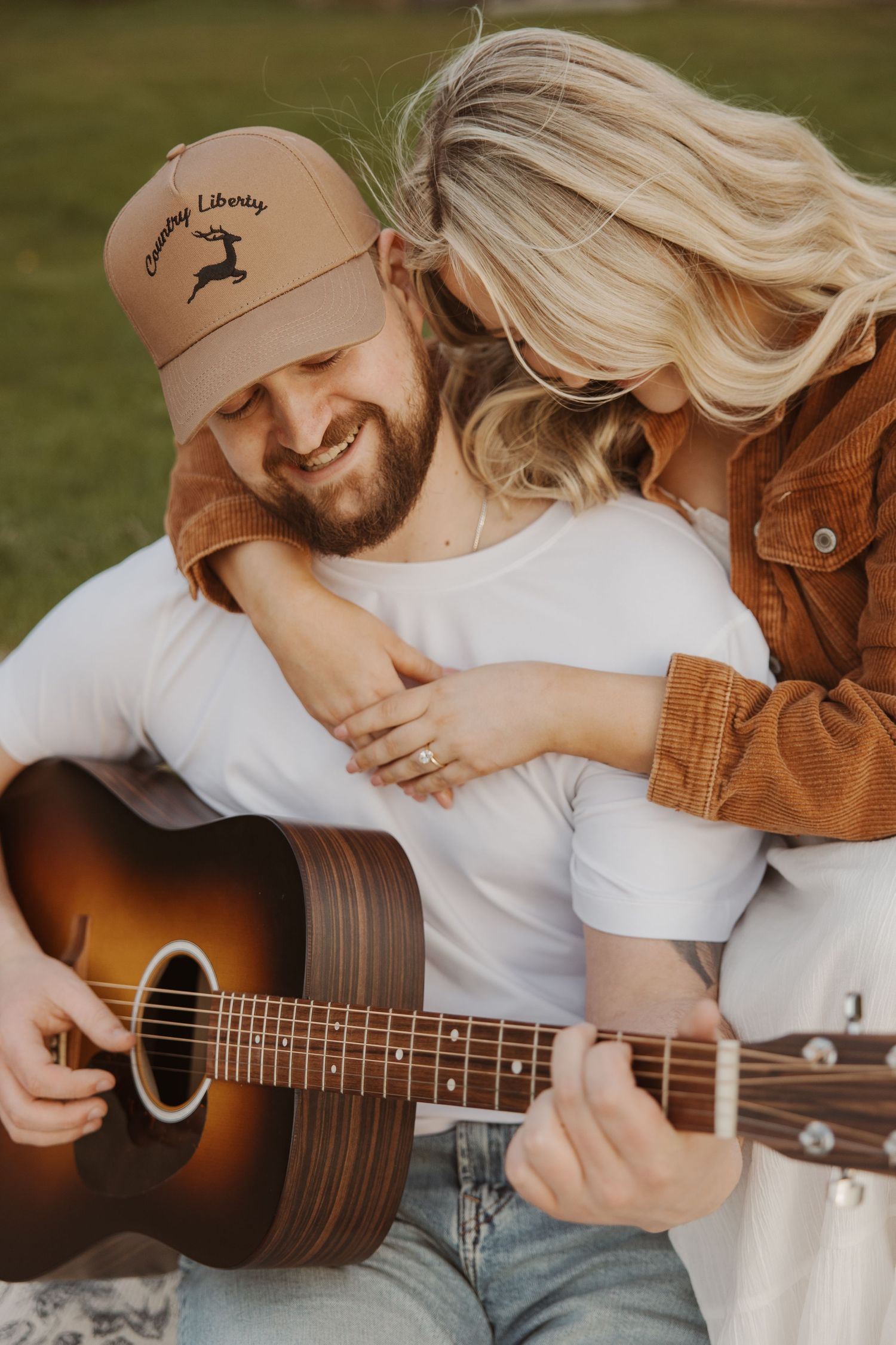 Woman hugging man from behind as he plays acoustic guitar on blanket.