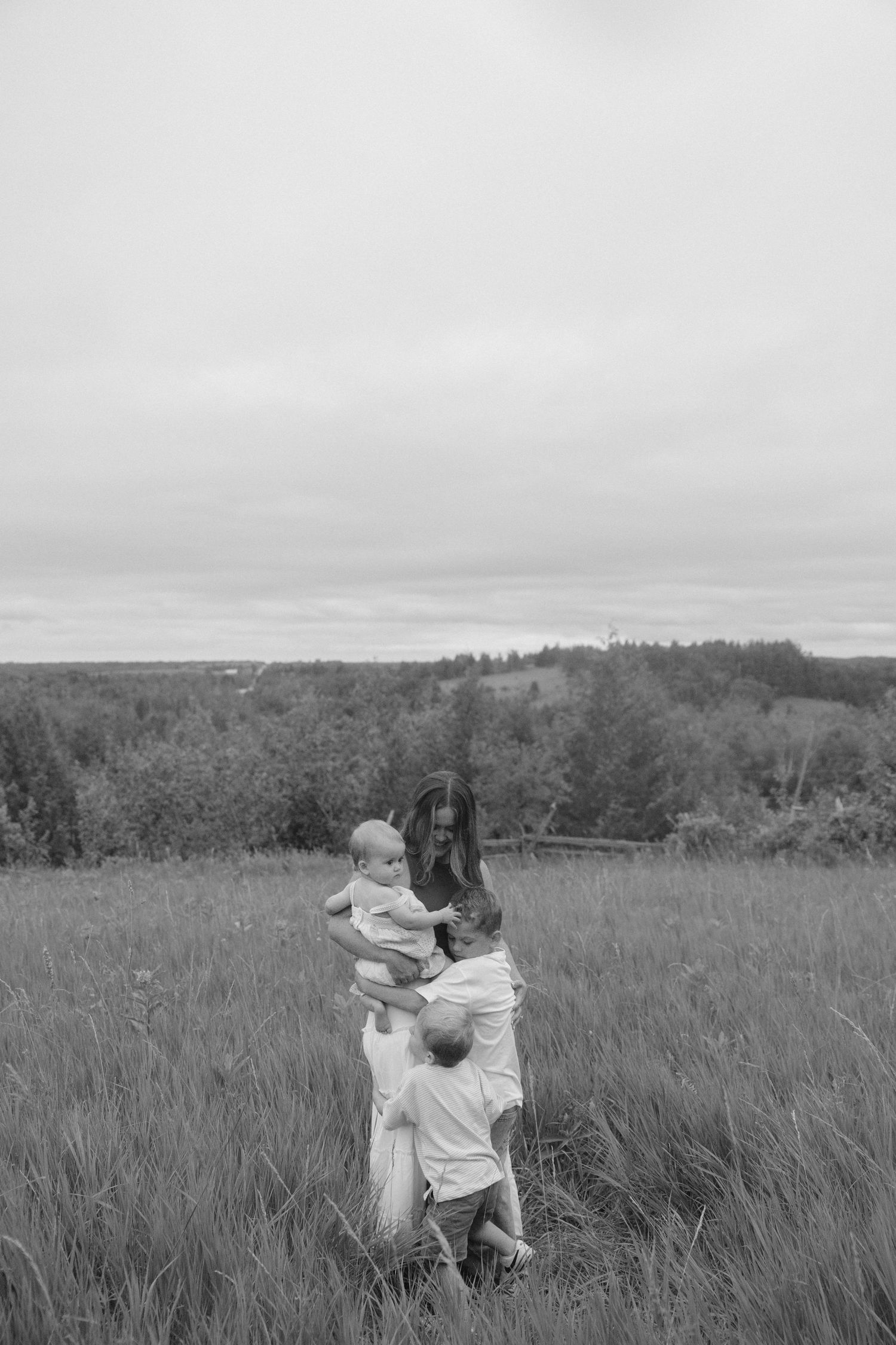 Black and white image of a mother with two young children playing in a grassy field.