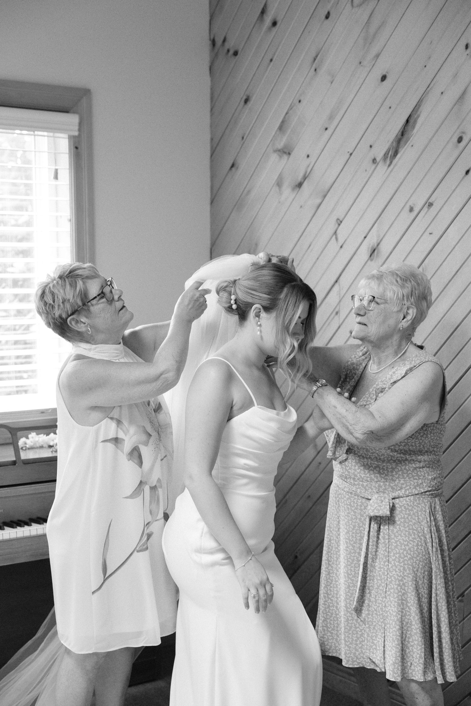 Black and white photo of two women helping bride with veil before wedding ceremony.