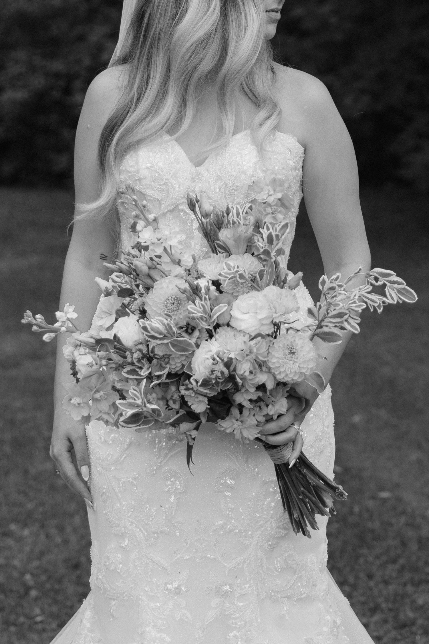 Black and white close-up of a bride in a lace gown holding a lush floral wedding bouquet.