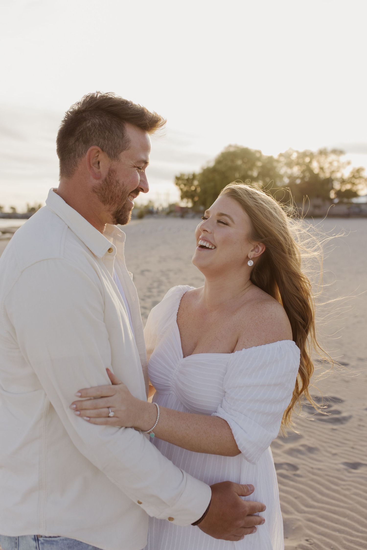 Happy couple embracing and laughing together on sandy beach at golden sunset.
