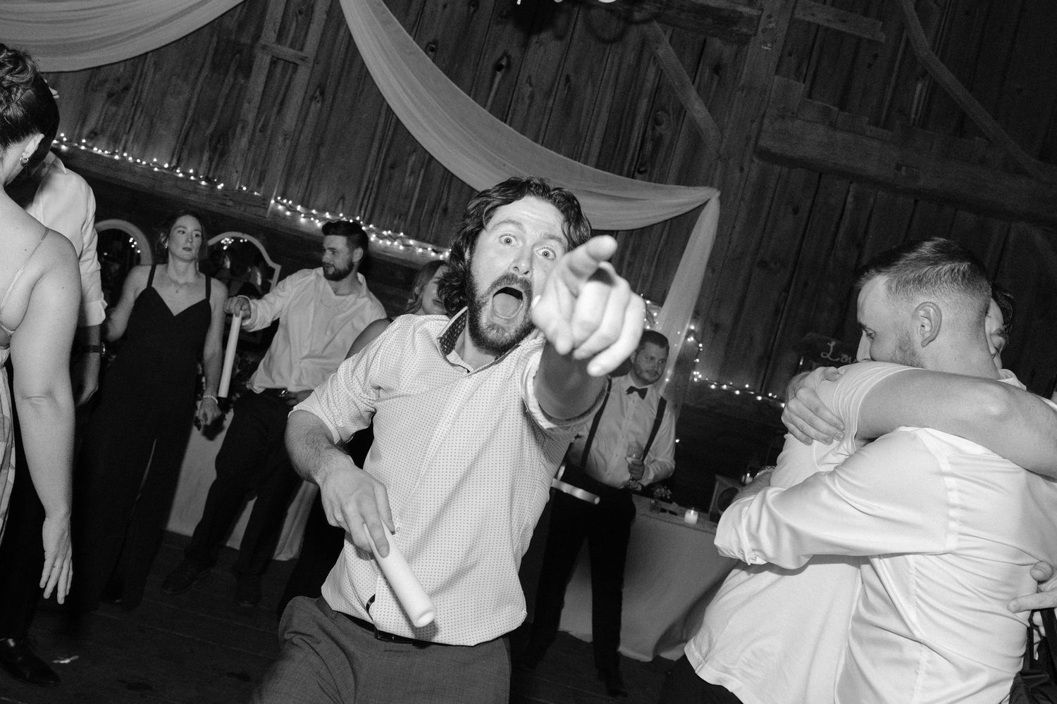 Energetic wedding guest pointing at camera with excited expression on barn reception dance floor.