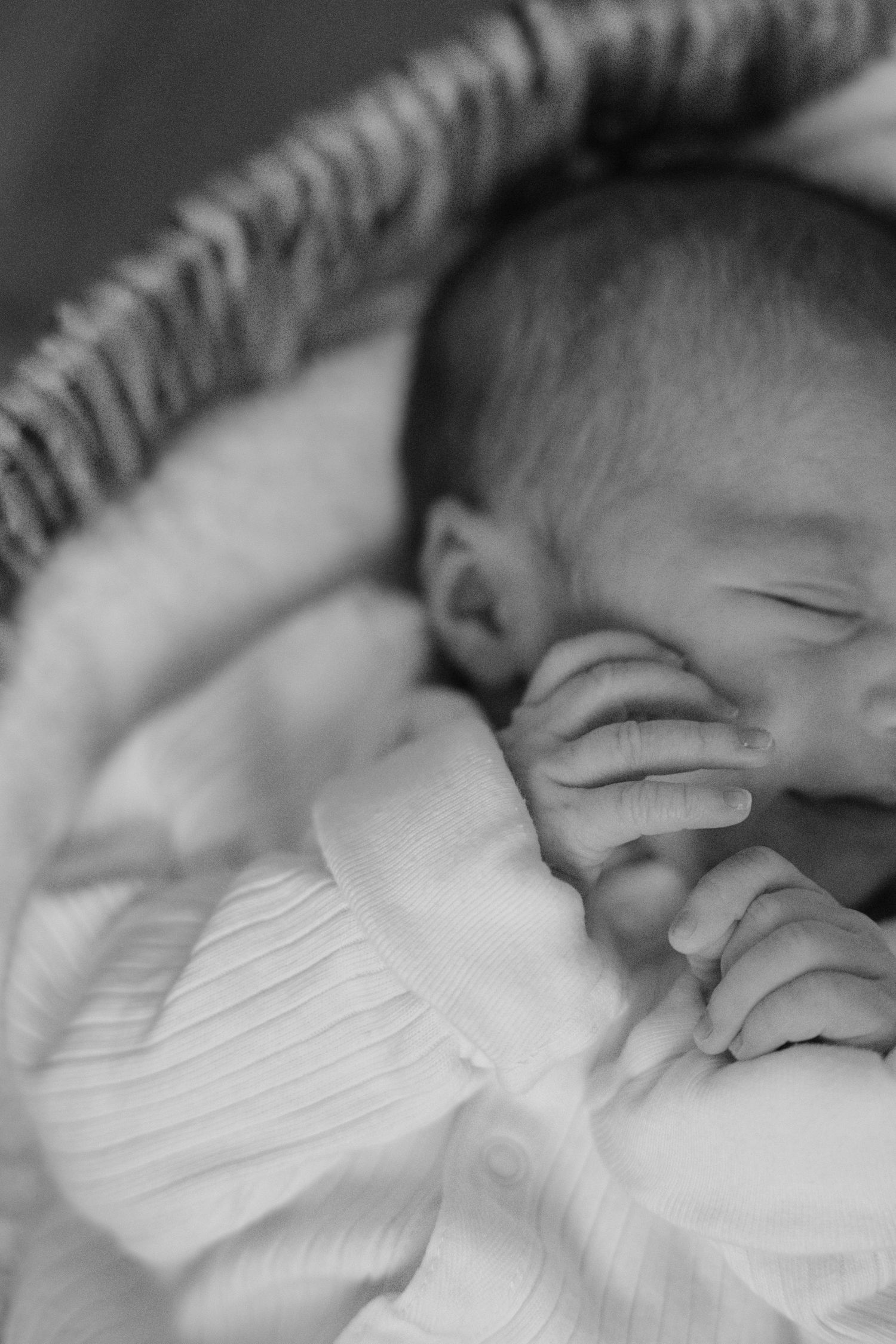 Black and white close-up of a peaceful sleeping newborn baby with tiny hands near face.