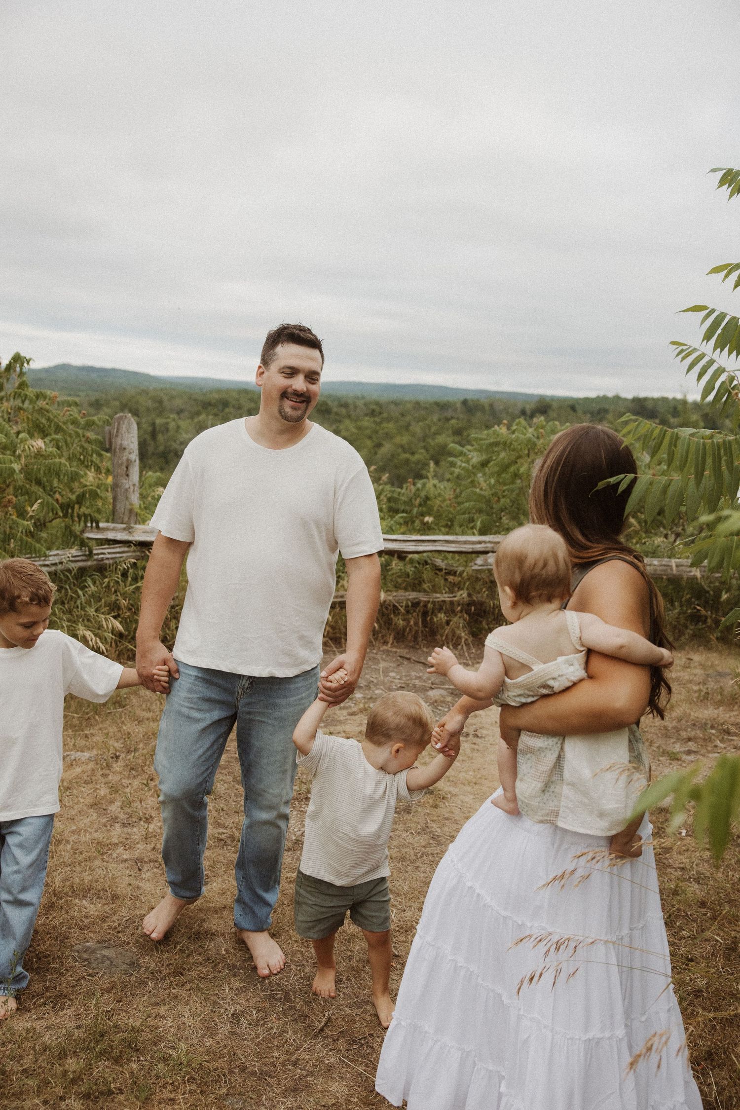 Happy family with young children holding hands outdoors in a scenic countryside garden setting.