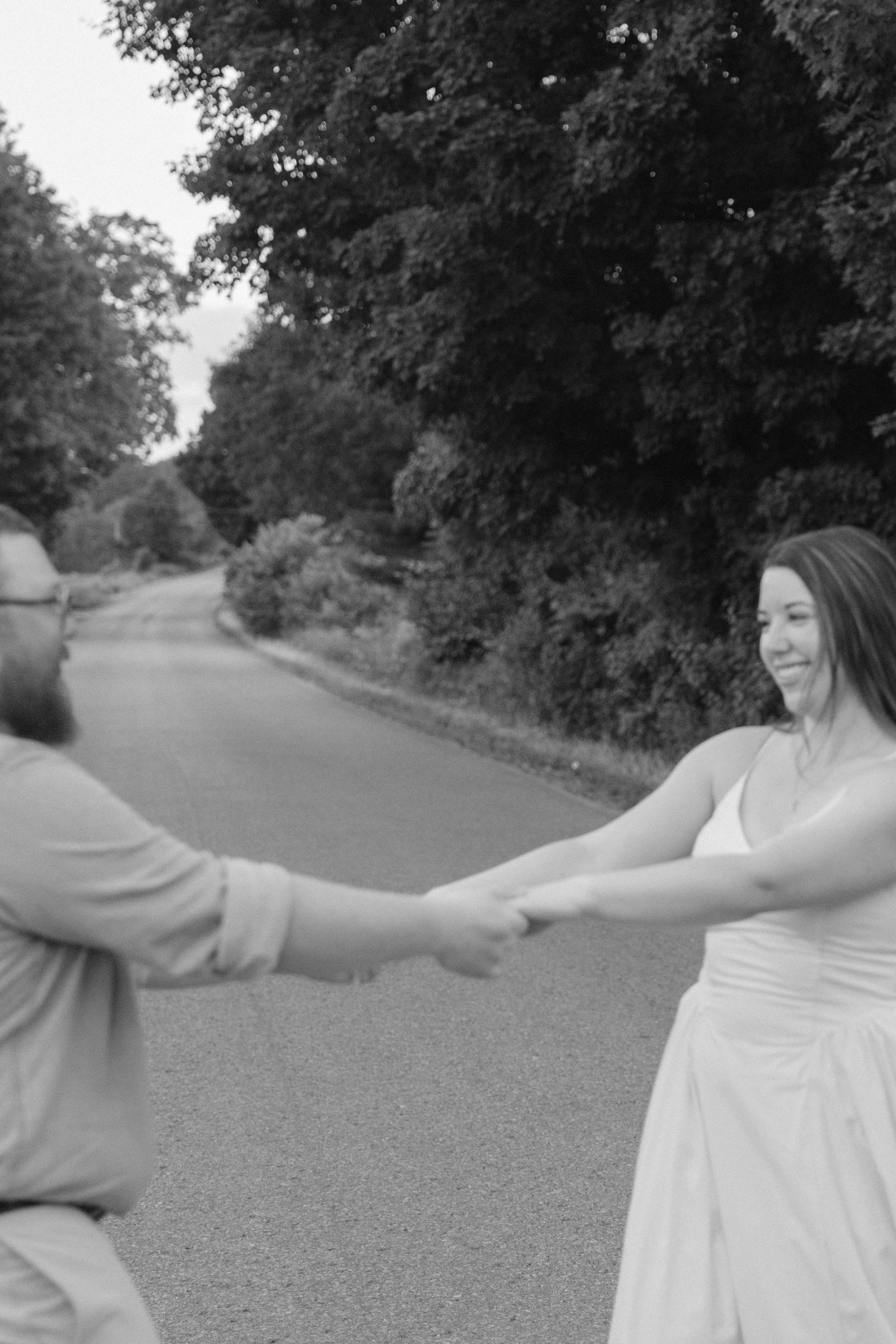 Black and white photo of couple holding hands on a tree-lined road.