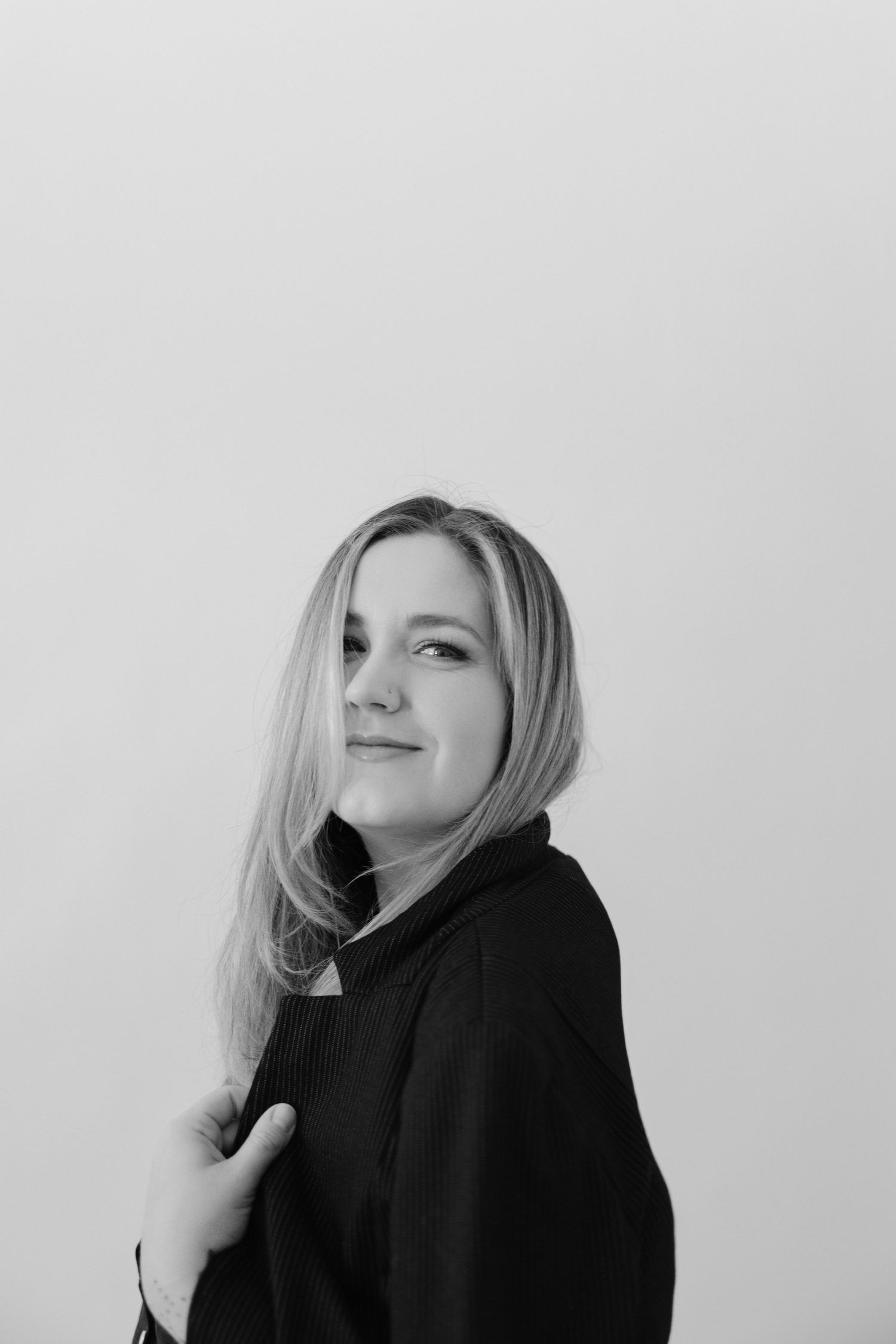 Black and white portrait of smiling blonde woman in black turtleneck sweater against white background.