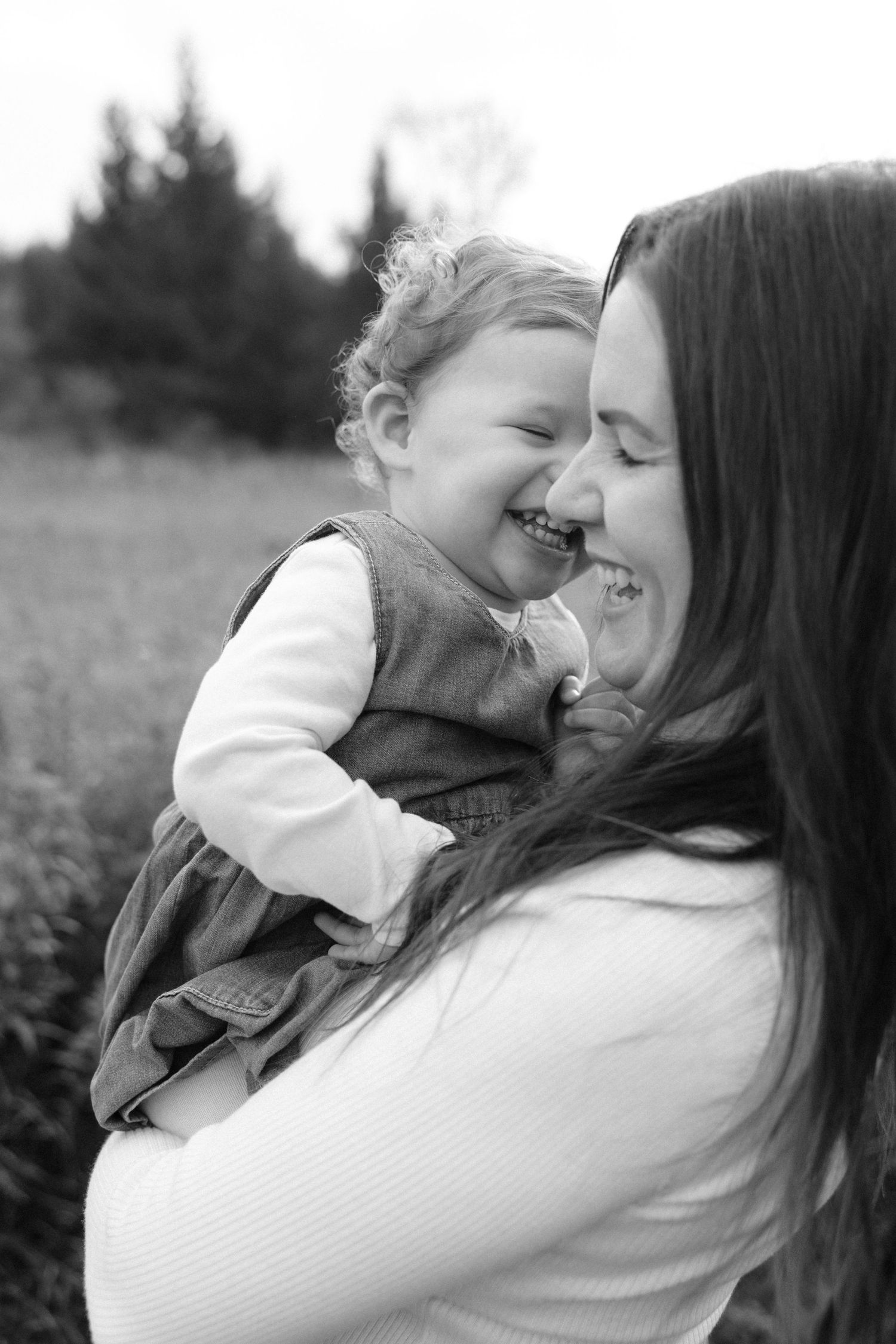 Black and white photo of a laughing toddler being held by her smiling mother outdoors.