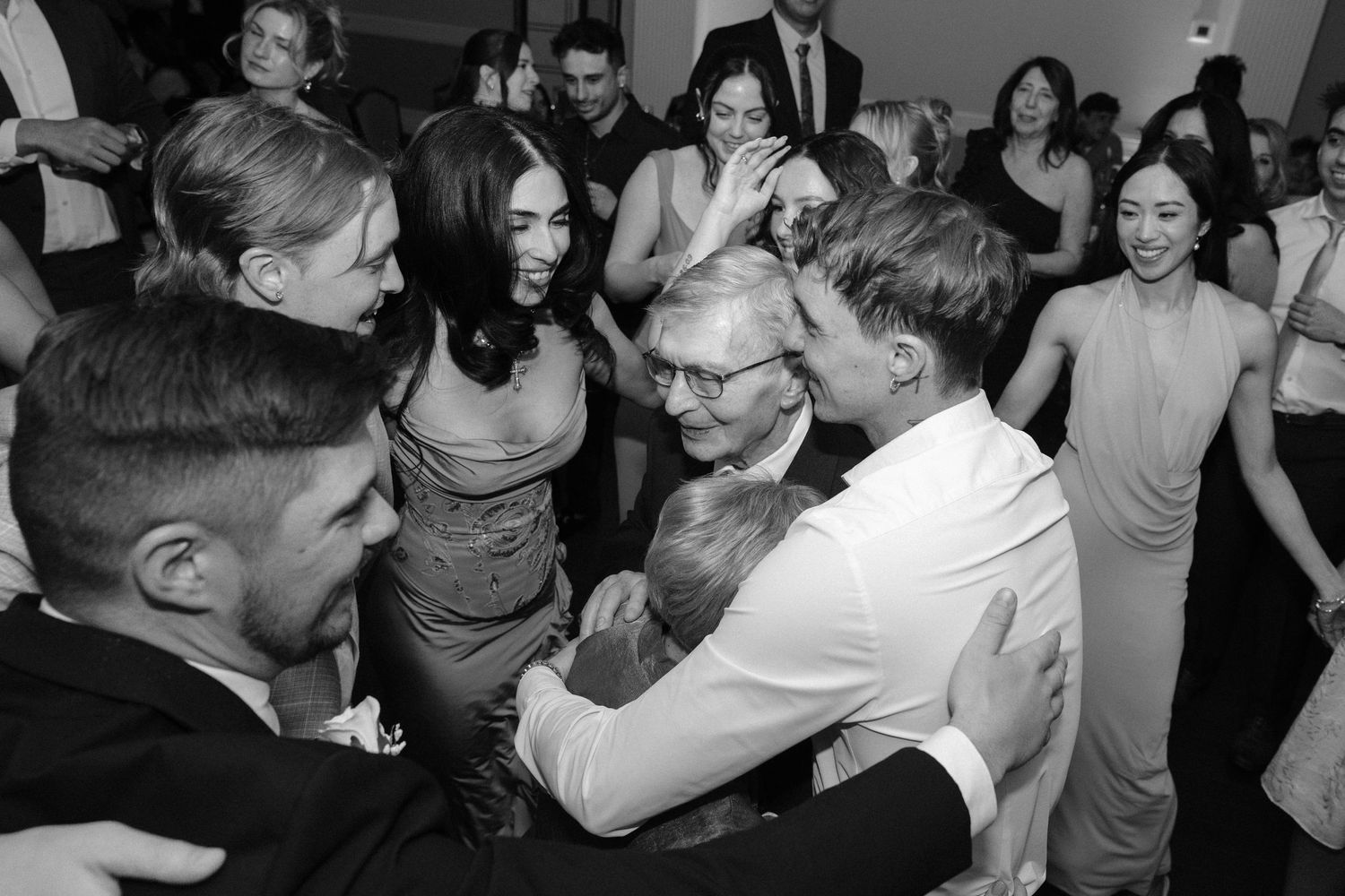 Black and white photo of guests dancing and embracing joyfully at an elegant wedding reception party.